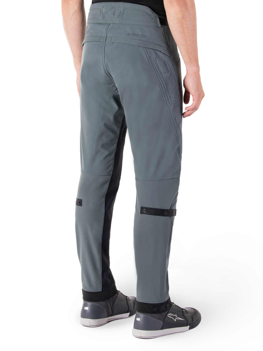 Alpinestars Alden Hose, Urban Grau, seitliche Rückansicht, Streetwear-inspirierte technische Motorradhose mit gesteppten Details an der Taille und schwarzen Wadenriemen, kombiniert mit grauen Motorradschuhen, moderne urbane Motorradausrüstung