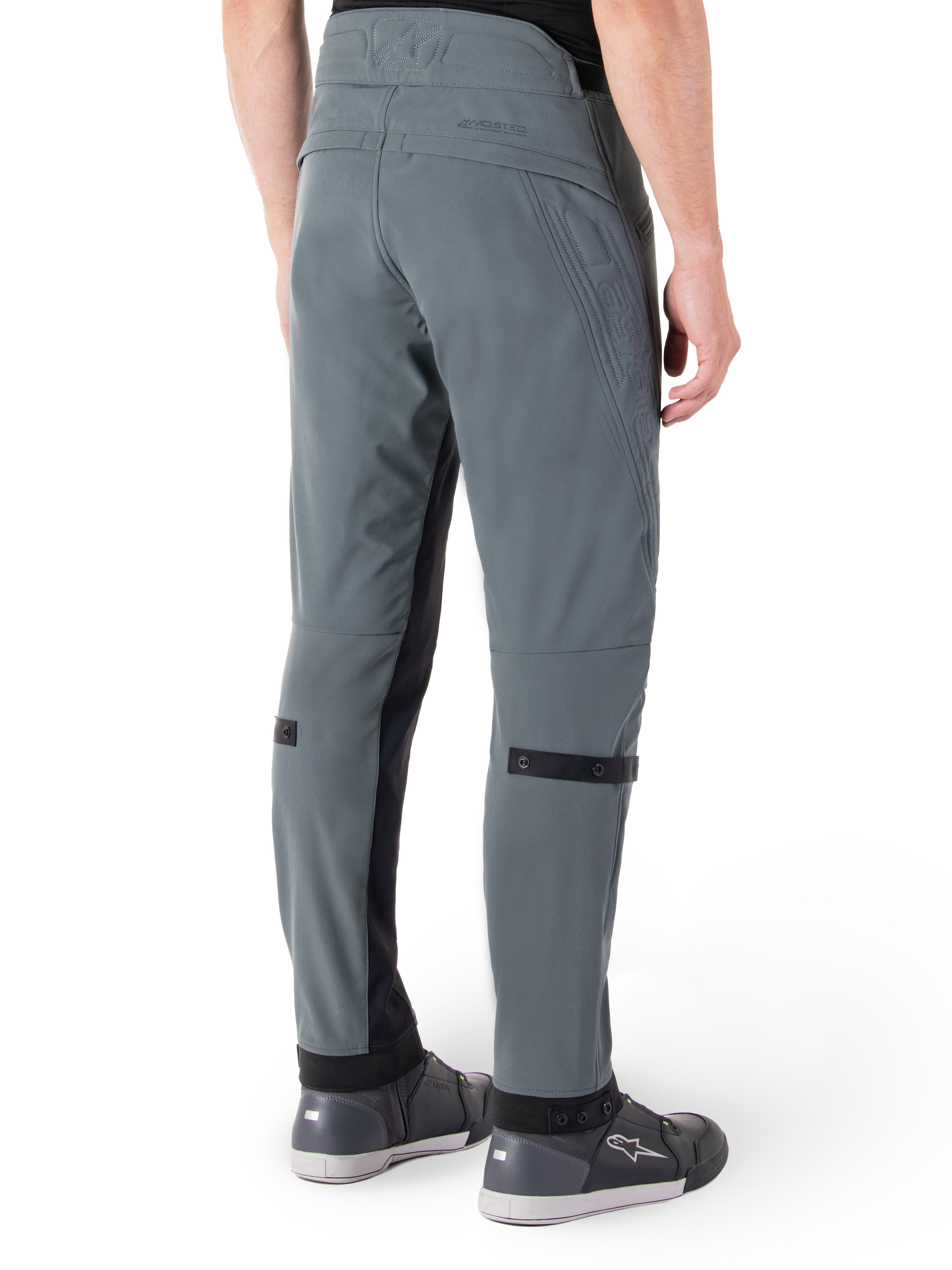 Alpinestars Alden Hose, Urban Grau, seitliche Rückansicht, Streetwear-inspirierte technische Motorradhose mit gesteppten Details an der Taille und schwarzen Wadenriemen, kombiniert mit grauen Motorradschuhen, moderne urbane Motorradausrüstung