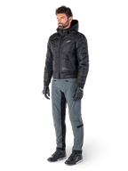 Alpinestars Alden Hose in Urban Gray, getragen von einem Model mit einer schwarzen gesteppten Kapuzenjacke, Handschuhen und Motorradschuhen, mit gesteppten Details an den Seiten und schwarzen Einsätzen an den Beininnenseiten, Streetwear-inspirierte urbane Motorradausrüstung