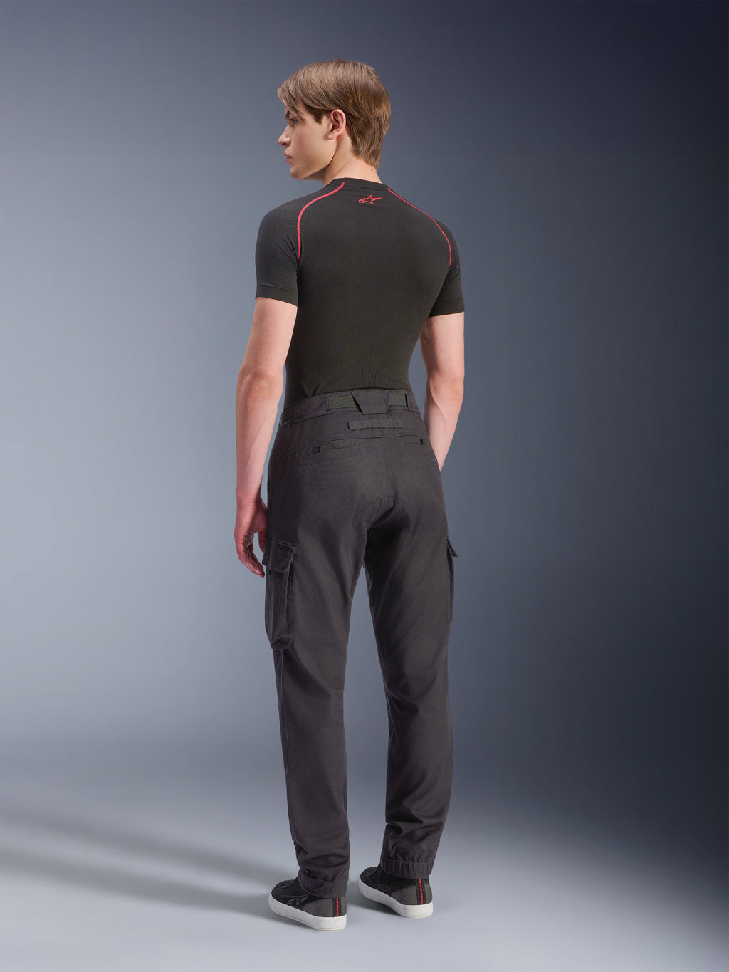 Alpinestars Flex-AST Cargo Pants, Black, urban motorcycle pants seen from the back, featuring cargo pockets and tapered legs with elasticated hems, worn with a black short-sleeve base layer and black sneakers, minimalist technical design.