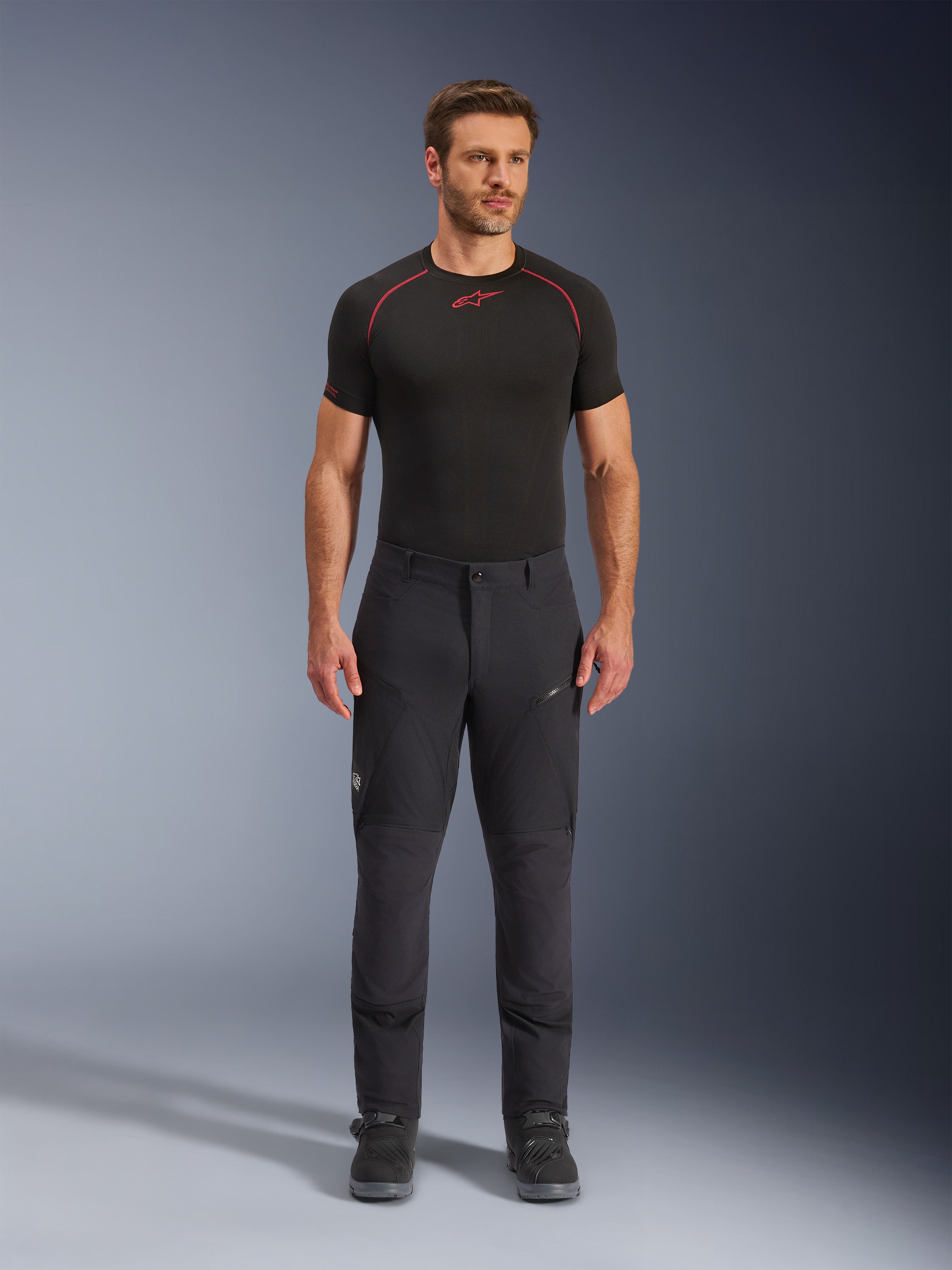 Alpinestars Flex-AST Explorer Hose, schwarze Adventure-Touring-Motorradhose, Mann in eng anliegender Textilhose mit Reißverschluss-Cargotaschen und verstärkten Einsätzen, kombiniert mit einem schwarzen Base-Layer und Motorradstiefeln, strapazierfähiger Schutz für Adventure-Fahrten