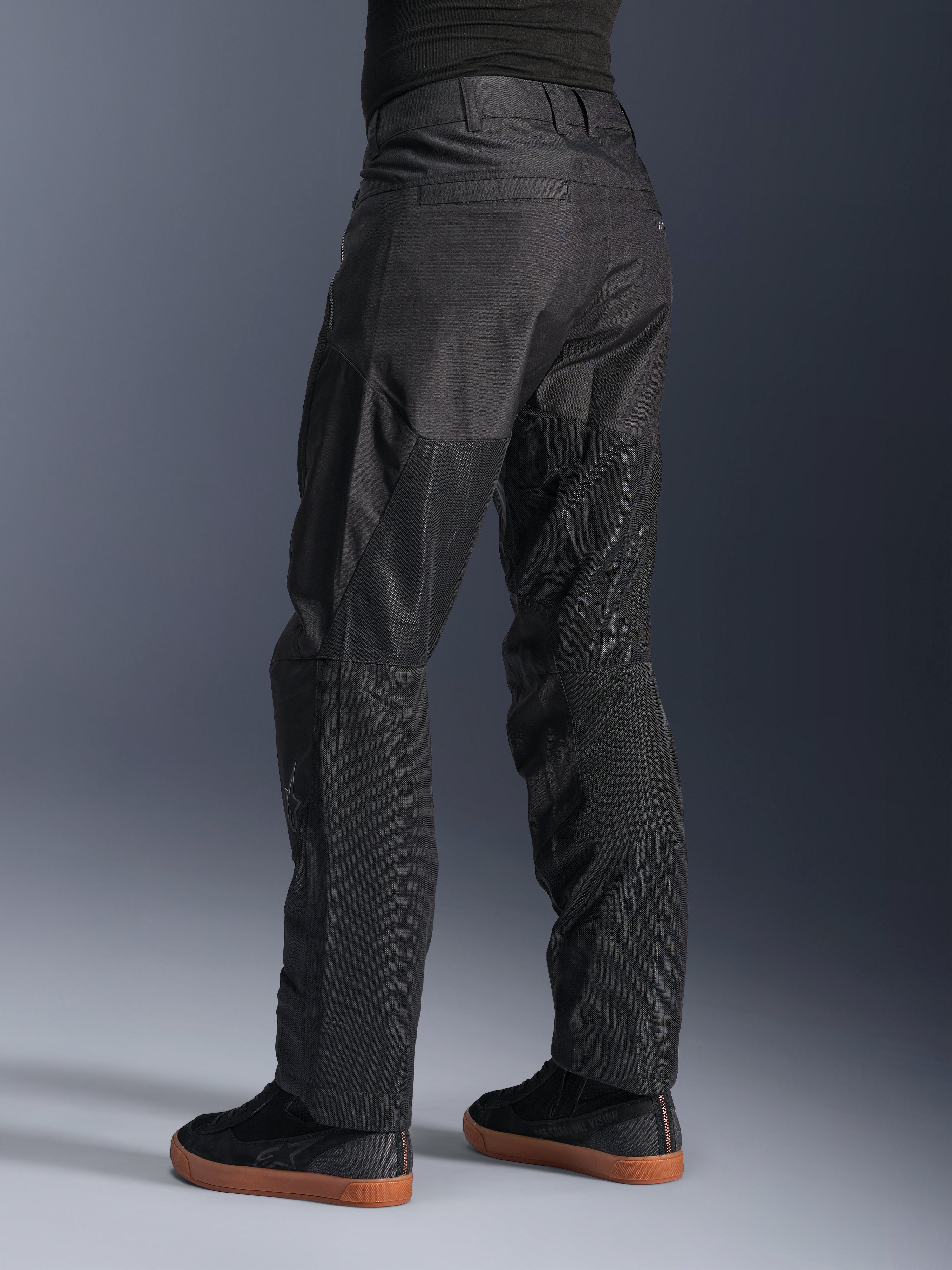 Alpinestars C-1 Air Hose, Urbane Motorradhose, Schwarz, Rückansicht mit großen Tech-Mesh-Einsätzen an der Beinrückseite zur Belüftung, schlichtes Design für die Stadt, getragen mit lässigen schwarzen Sneakern.