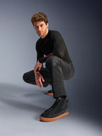 Alpinestars C-1 Air Hose, Urbane Motorradhose, Schwarz, Modell hockend in einer Studio-Umgebung, kombiniert mit schwarzem Langarm-Oberteil und schwarzen Sneakern mit hellbraunen Sohlen, mit atmungsaktiven Mesh-Einsätzen und modernem urbanen Stil