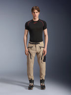 Männliches Model in Alpinestars Acteon Hose in Sand, kombiniert mit einem schwarzen kurzärmeligen Base Layer und schwarzen technischen Stiefeln, mit Cargotaschen mit schwarzen Reißverschlüssen und einer schmal zulaufenden Passform, zeitgemäße urbane Motorradausrüstung