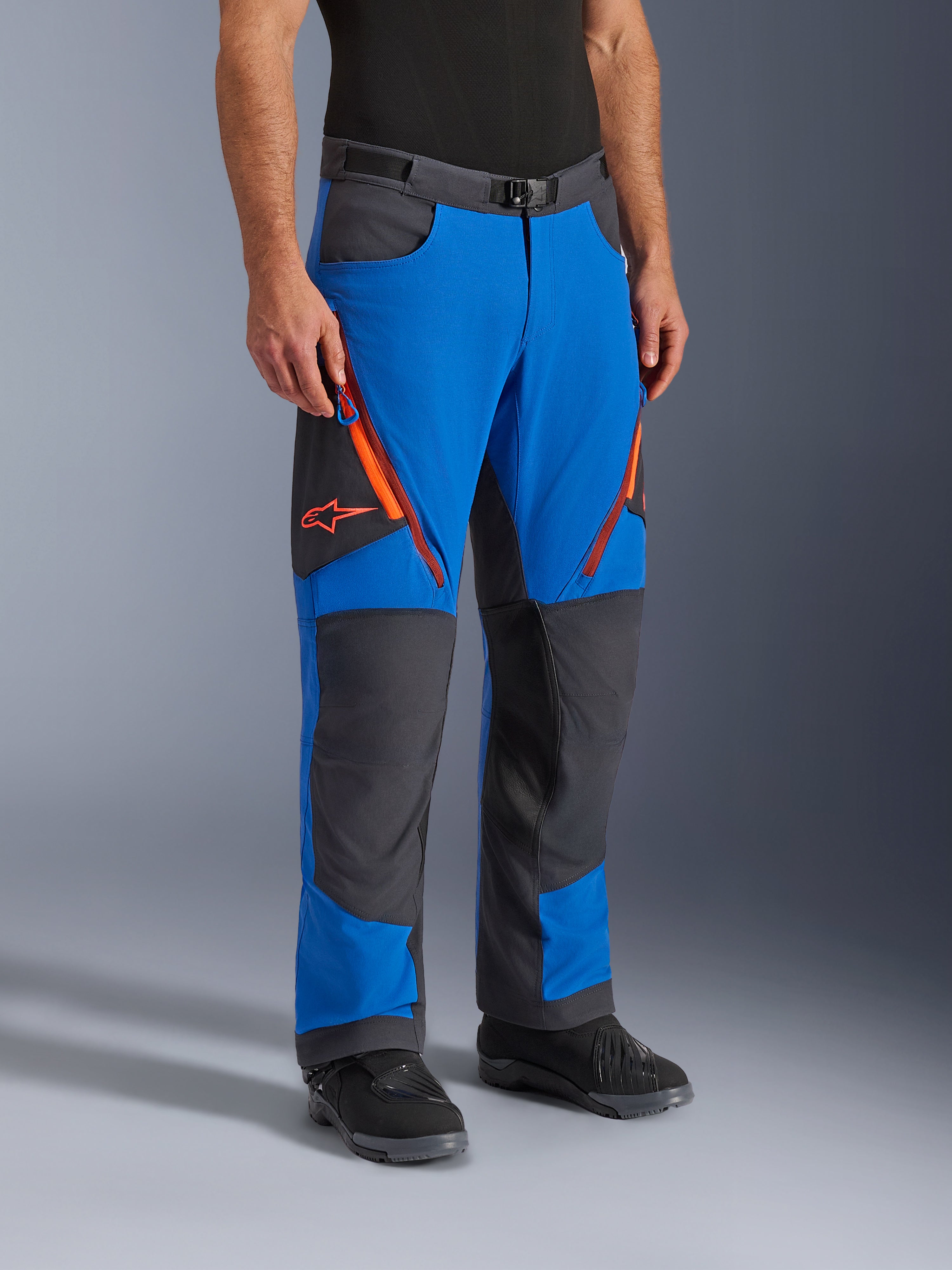 Alpinestars Maxdura Dual Pants, Adventure-Motorradhose, Königsblau und Dunkelgrau mit orangen Akzenten, mit Oberschenkelbelüftungen mit Reißverschluss, verstärkten Kniepaneelen und einem Gürtel mit Magnetschnalle, technisches Über-Stiefel-Design für Dual-Sport-Fahrten.