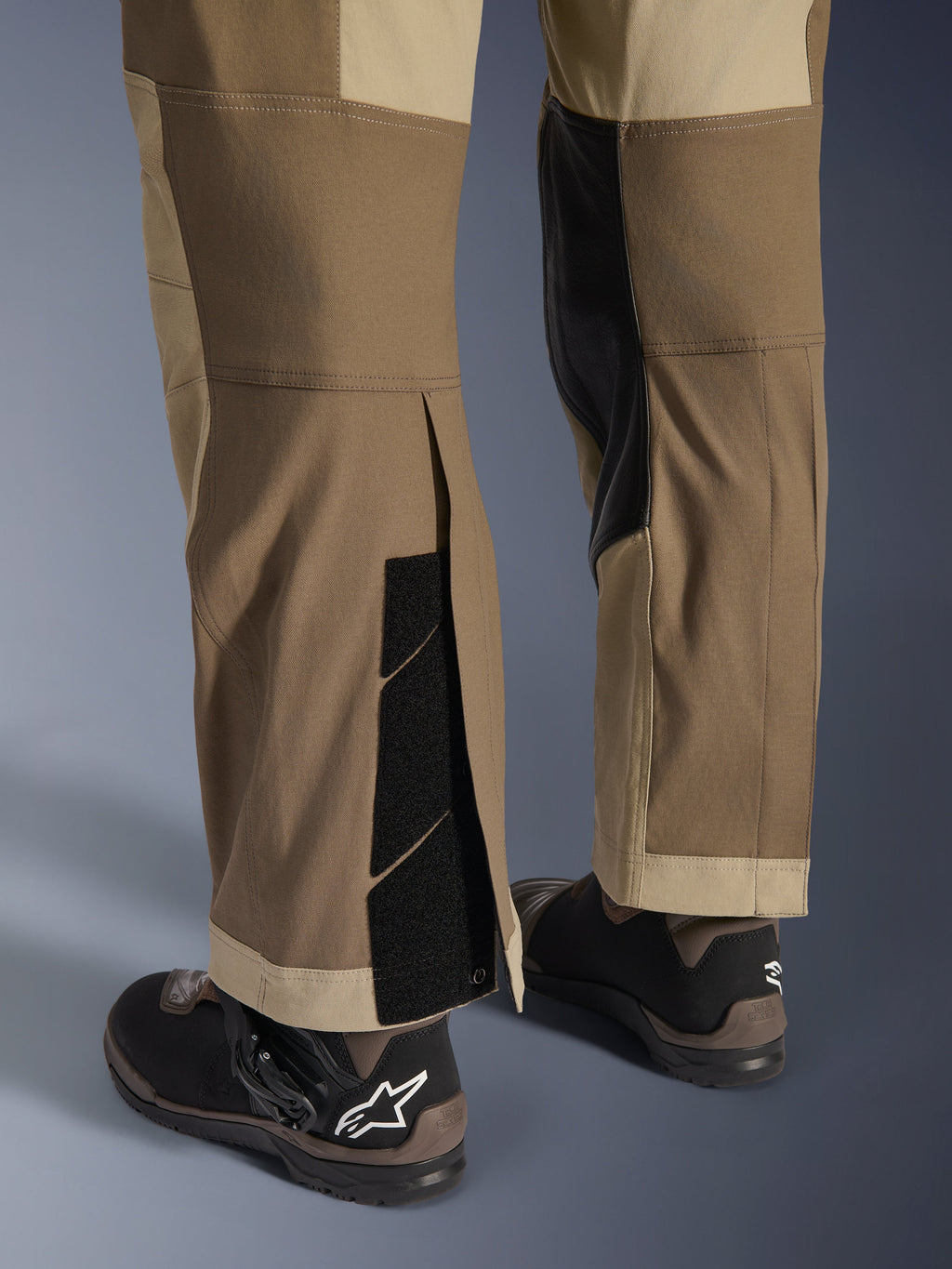 Alpinestars Maxdura Dual Hose in Walnut Aluminum, Detailansicht von Unterschenkel und Saum mit Über-den-Stiefel-Design, verstellbare Klettverschlüsse und verstärkte Innenpaneele, kombiniert mit schwarzen Motorradstiefeln.