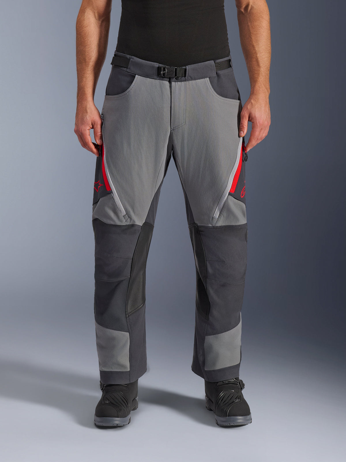 Alpinestars Maxdura Dual Hose, Adventure-Motorradhose, Dunkelgrau und Tiefgrau mit roten Akzenten, Vorderansicht mit Reißverschluss-Belüftungsöffnungen an den Oberschenkeln, Gürtel mit Magnetschnalle und verstärkten Kniepaneelen, Over-Boot-Design für Dual-Sport-Fahrten.