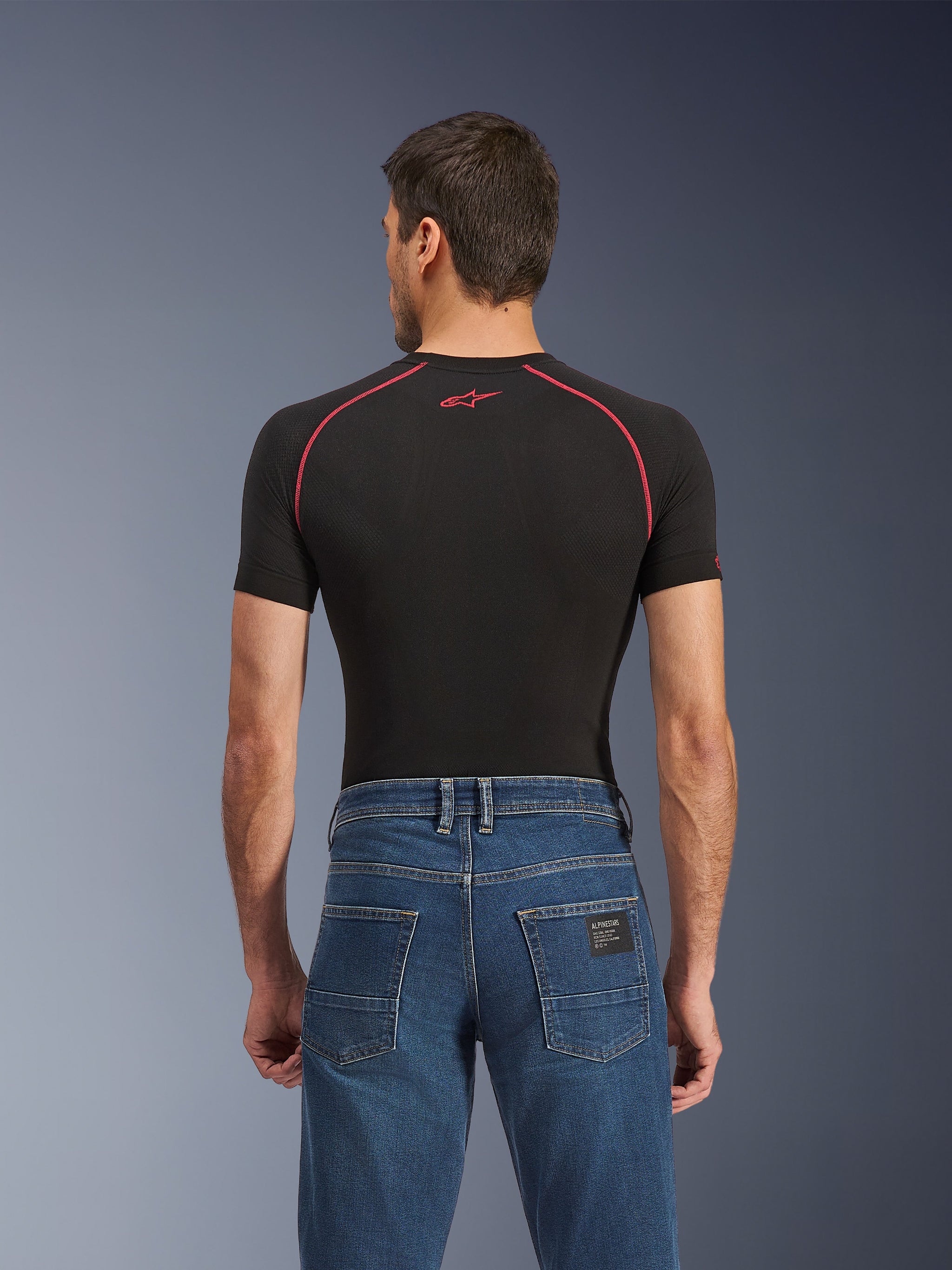 Alpinestars Flex-AST 5 Denim-Hose, Indigo Washed, Rückansicht zeigt reguläre konische Passform, getragen mit schwarzem kurzärmeligem Base-Layer mit roten Nähten, lässige urbane Motorradjeans.