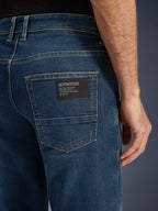 Alpinestars Flex-AST 5 Denim Pants, Urban Motorcycle Jeans, Indigo Washed, close-up of the back pocket featuring a black Alpinestars logo patch with 'One Goal. One Vision.' text, contrast gold stitching, and monolayer denim texture