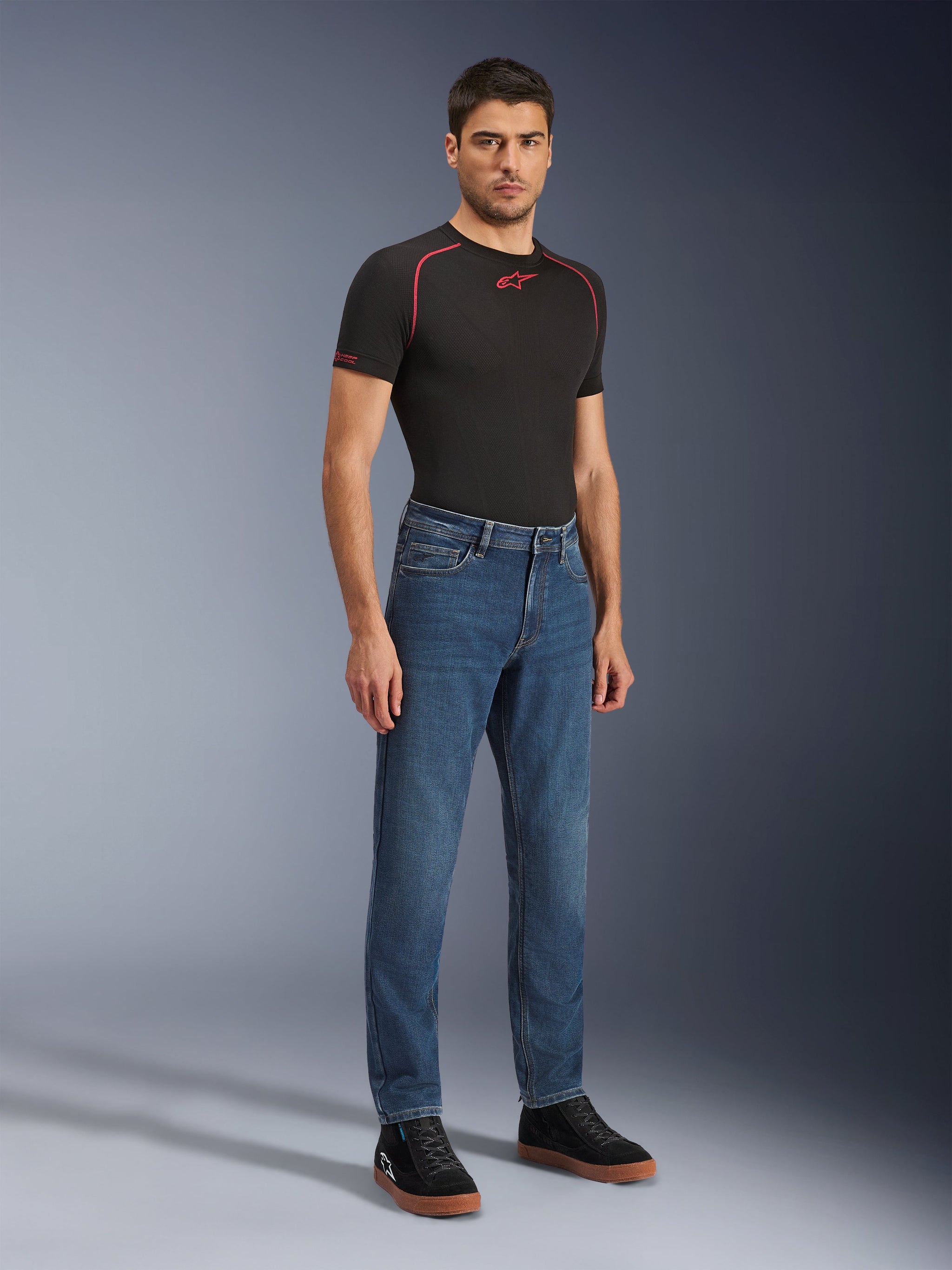 Alpinestars Flex-AST 5 Denim-Hose, Motorradjeans in Indigo Washed, moderne konische Passform, getragen von einem männlichen Model mit einem schwarzen Performance-T-Shirt und schwarzen Sneakern, lässige urbane Motorradbekleidung