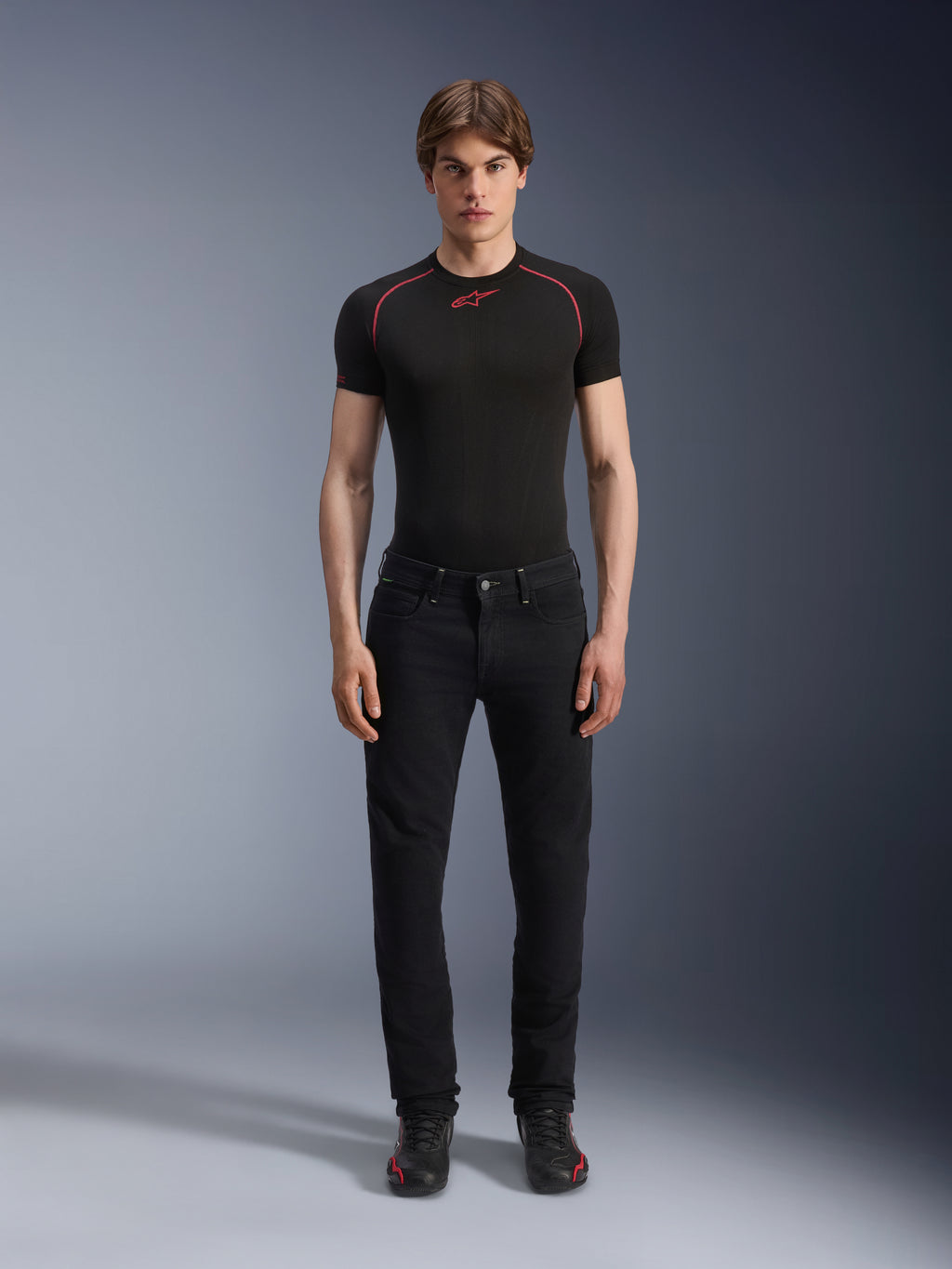 Alpinestars Copper V3 Denim Hose in Black Rinse, reguläre, bequeme Passform mit geradem Bein, getragen von einem männlichen Model mit einem schwarzen Baselayer-T-Shirt mit roten Kontrastnähten und schwarzen Motorrad-Sneakern, urbanes Motorrad-Outfit
