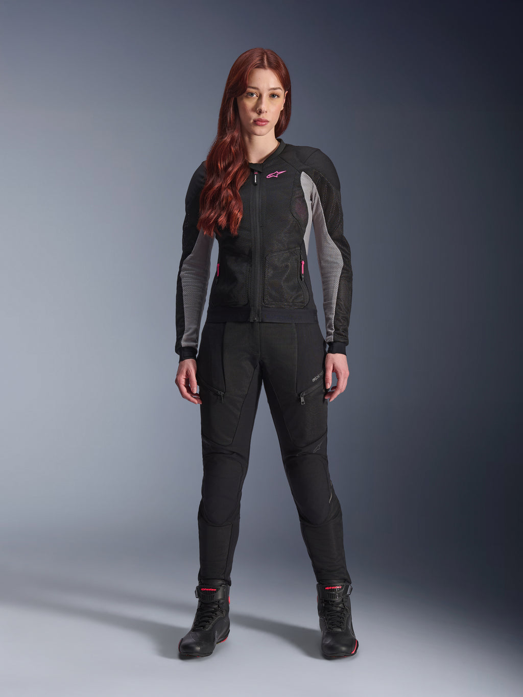 Alpinestars Stella Troop-Air Jacket and Pants, Women's Motorcycle Riding Gear, Black with Ash Gray and Pink Fluo accents, worn by a female model with red hair, featuring mesh ventilation and protective design, studio standing pose.