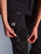 Nahaufnahme der Alpinestars Stella Flex-AST Explorer Hose in Schwarz, zeigt die externe Protektorentasche beim Einsetzen des Nucleon Flex Plus Knieprotektors, Detail der Wabenstruktur, „ALL TERRA“ Branding auf dem Oberschenkel, funktionale Adventure-Textilausrüstung für Damen