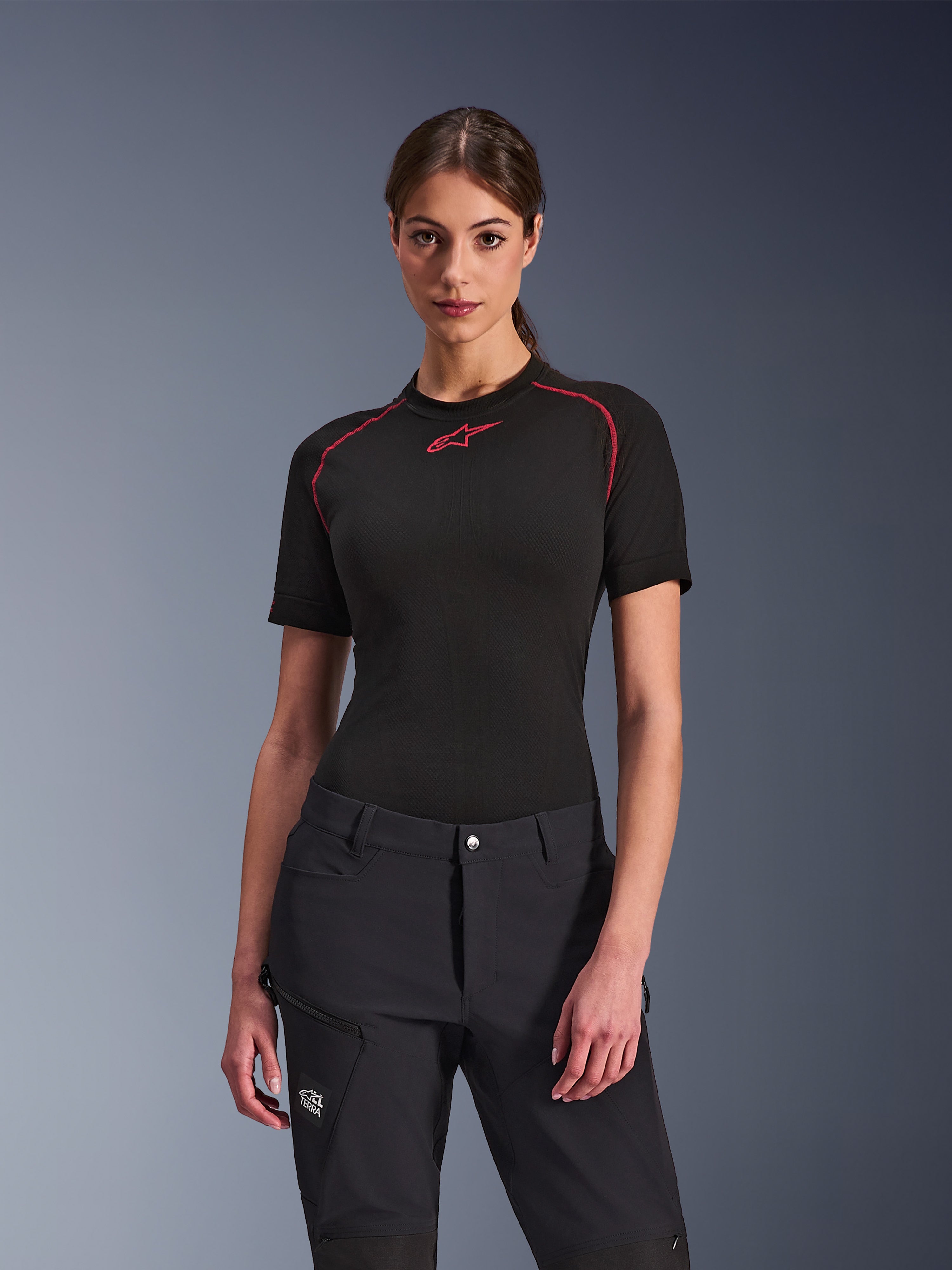Frau in Alpinestars Stella Flex-AST Explorer Hose in Schwarz, kombiniert mit einem schwarzen kurzärmeligen Base Layer mit roten Akzenten, Adventure-Fahrbekleidung mit Cargo-Taschen und All Terra-Branding