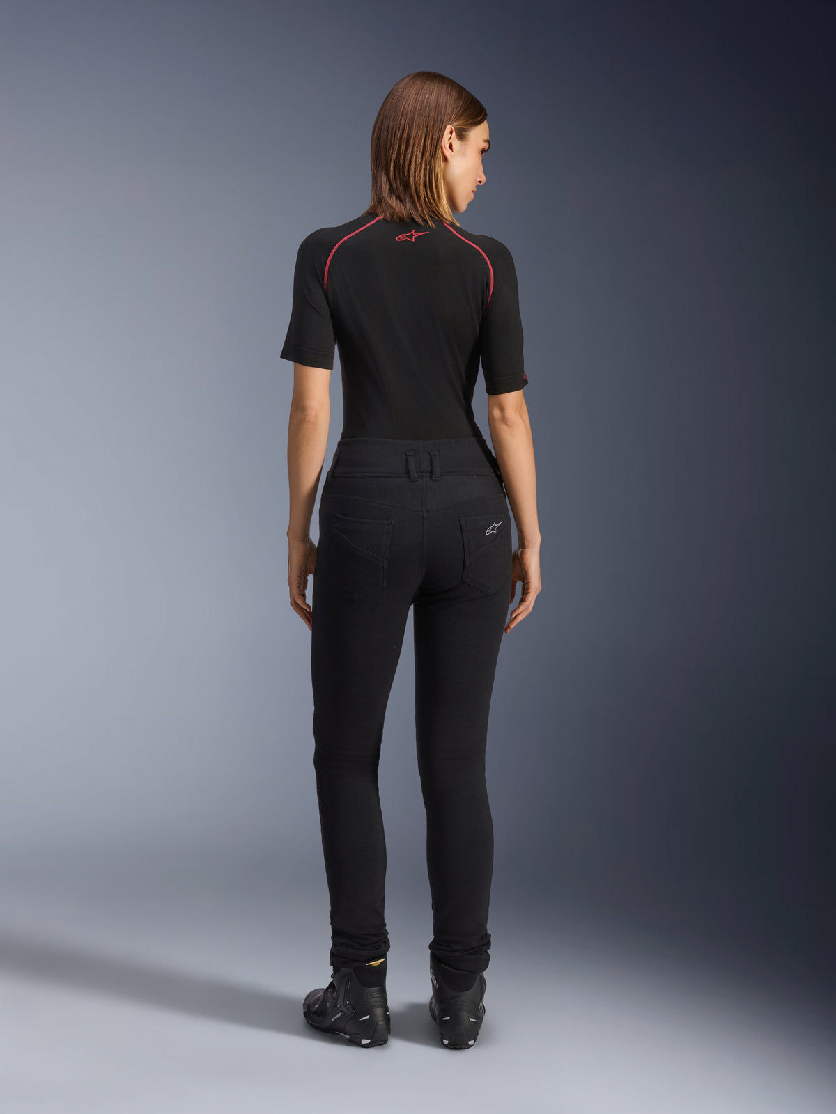 Alpinestars Women's Banshee Leggings, Black motorcycle leggings, back view showing figure-hugging fit and anatomical stretch fabric, featuring back pockets and logo detail, worn with a black base layer and riding shoes, urban motorcycle gear for women