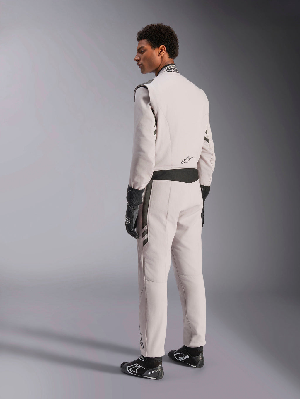 Alpinestars GP Race V3 Suit FIA, Silver Anthracite racing suit, side and back view, worn with black racing gloves and boots, featuring dark gray accents on the waist and shoulders, professional auto racing protective apparel.