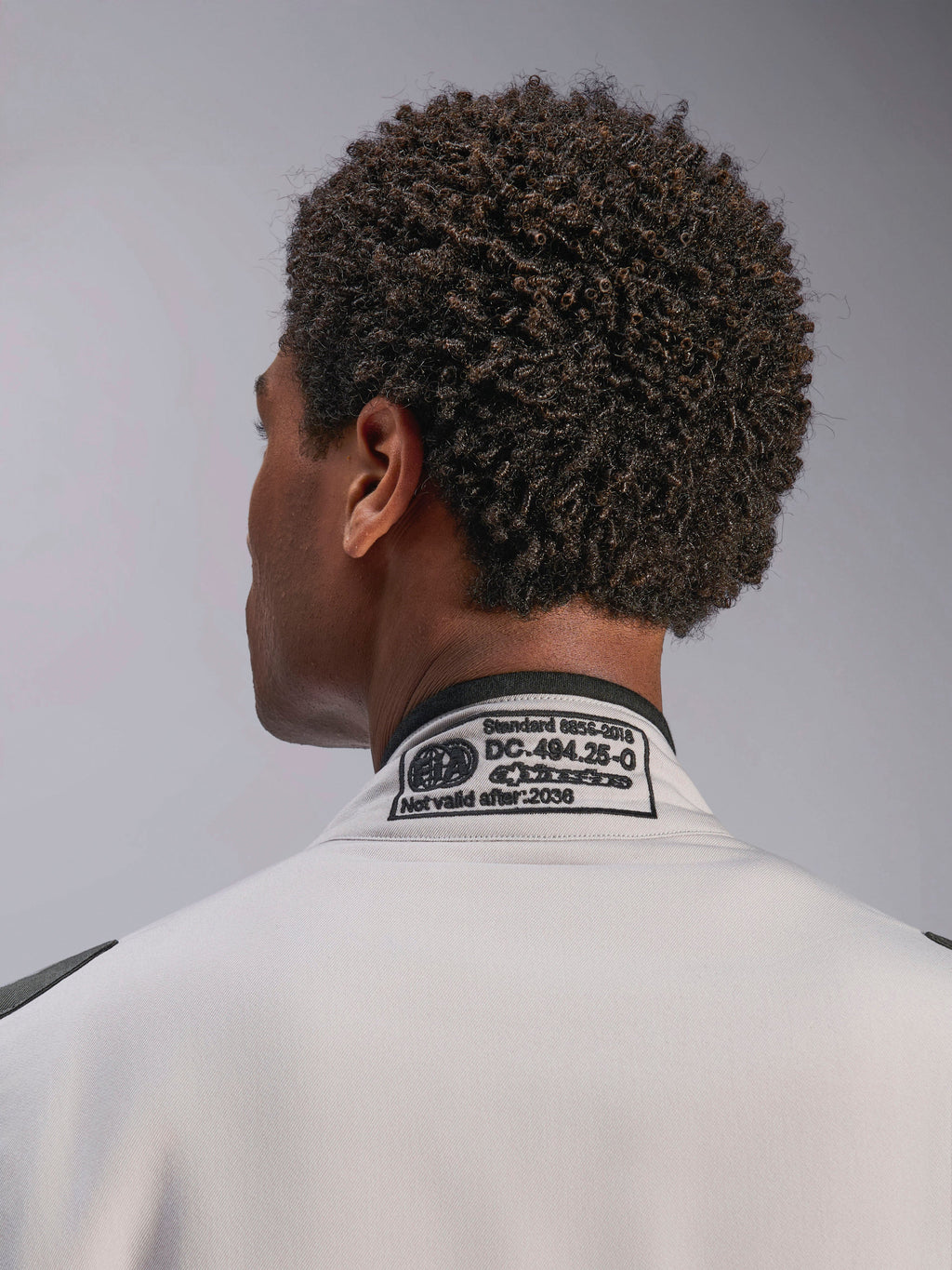 Alpinestars GP Race V3 Suit FIA, Silver Anthracite, close-up of the back collar featuring the embroidered FIA 8856-2018 certification label, detailing safety compliance for auto racing gear