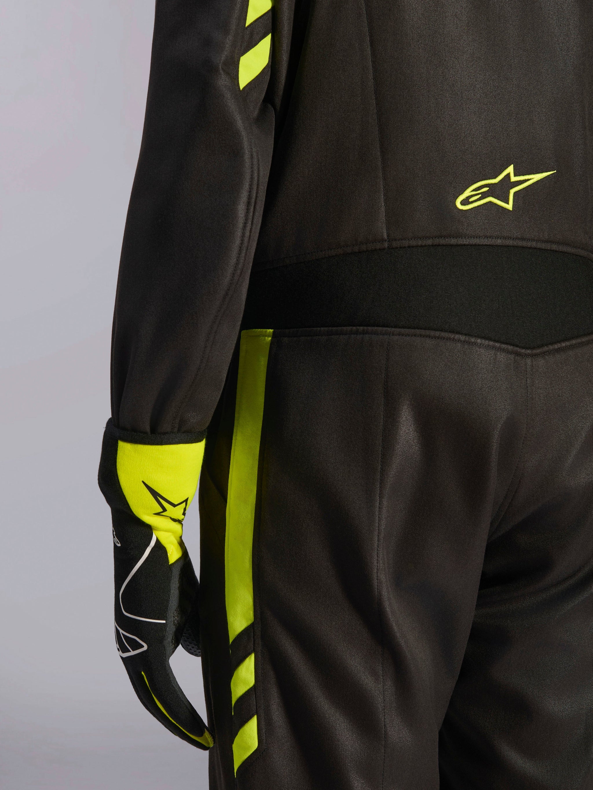 Alpinestars GP Race V3 Suit FIA, Black and Yellow Fluo, close-up detail of the waist and side leg, featuring aramidic stretch panels and matching racing glove, professional auto racing gear