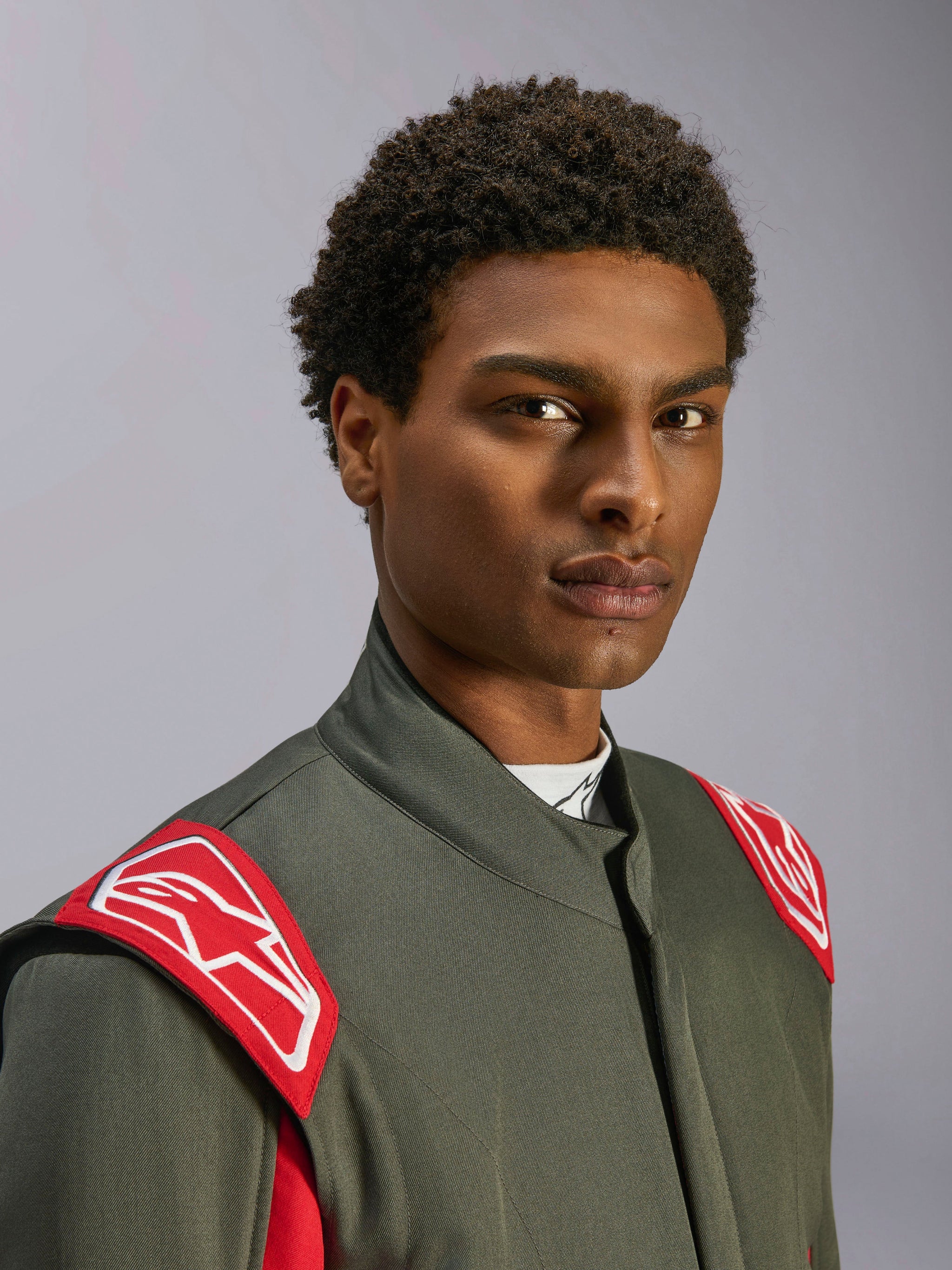 Alpinestars GP Race V3 Anzug FIA, Autorennanzug, Anthrazit-Rot, Nahaufnahme des Oberkörpers und Kopfes, mit roten Schulter-Epauletten mit weißem Alpinestars-Logo, hohem Kragen und grauem Twill-Material