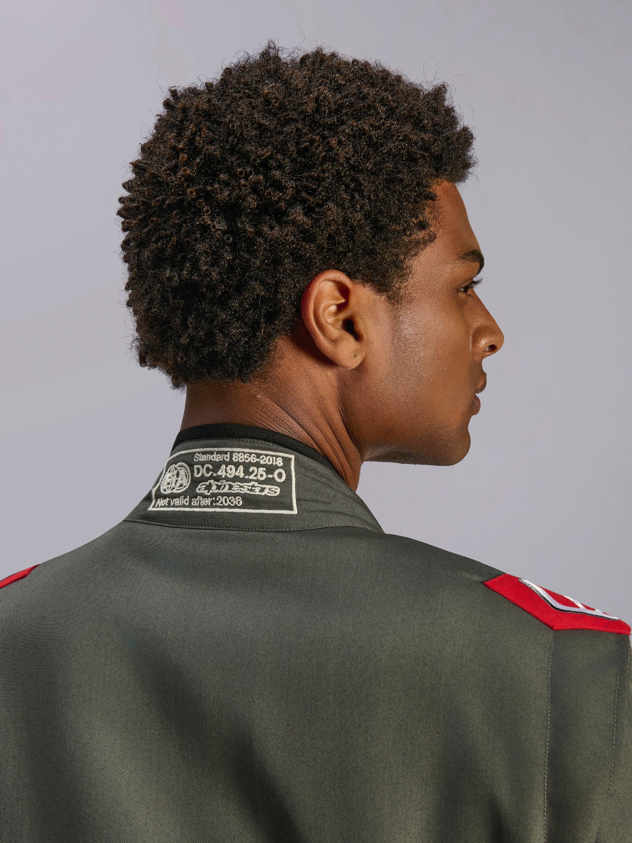 Alpinestars GP Race V3 Anzug FIA, Rennanzug in Anthrazit-Rot, Nahaufnahme des Rückenkragens mit FIA 8856-2018 Zertifizierungsetikett und roten Schulter-Epauletten, Detailansicht professioneller Motorsportbekleidung.