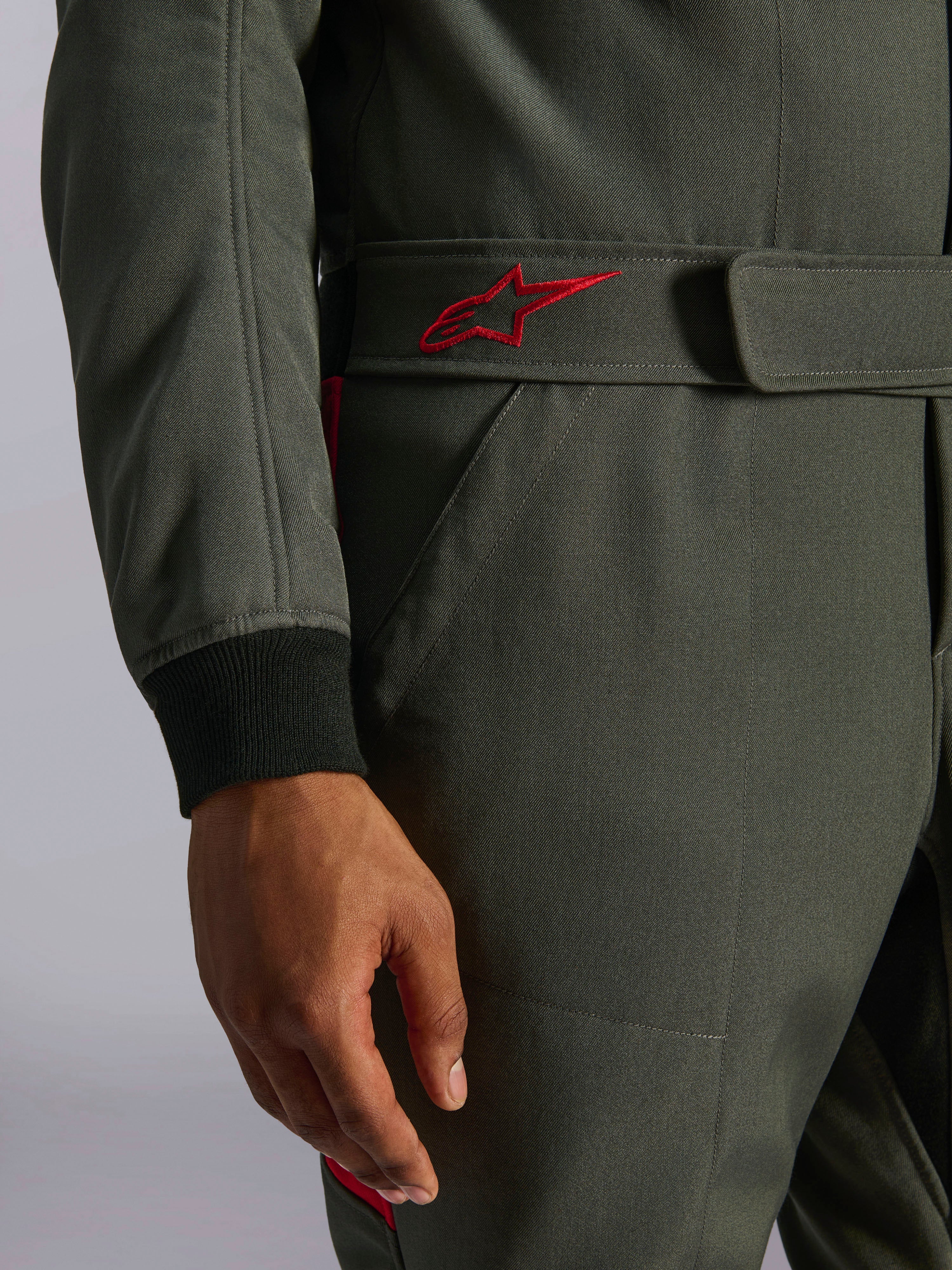 Alpinestars GP Race V3 Anzug FIA, Auto-Rennanzug, Anthrazit-Rot, Nahaufnahme des verstellbaren Gürtelbunds mit rot besticktem Logo und schwarzem geripptem Ärmelbündchen auf strukturiertem Twill-Gewebe