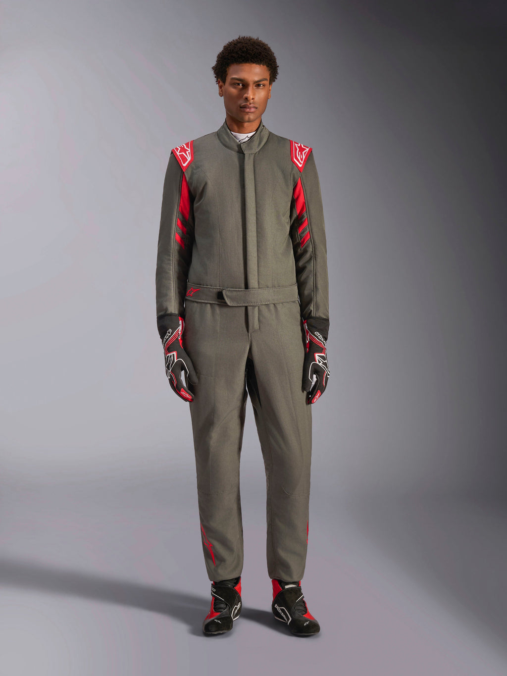 Alpinestars GP Race V3 Anzug FIA, Auto-Rennanzug, Anthrazit-Rot, getragen von einem männlichen Model mit passenden Handschuhen und Stiefeln, mit roten Schulter-Epauletten und Branding, professionelle Motorsportausrüstung für Performance-Fahren.