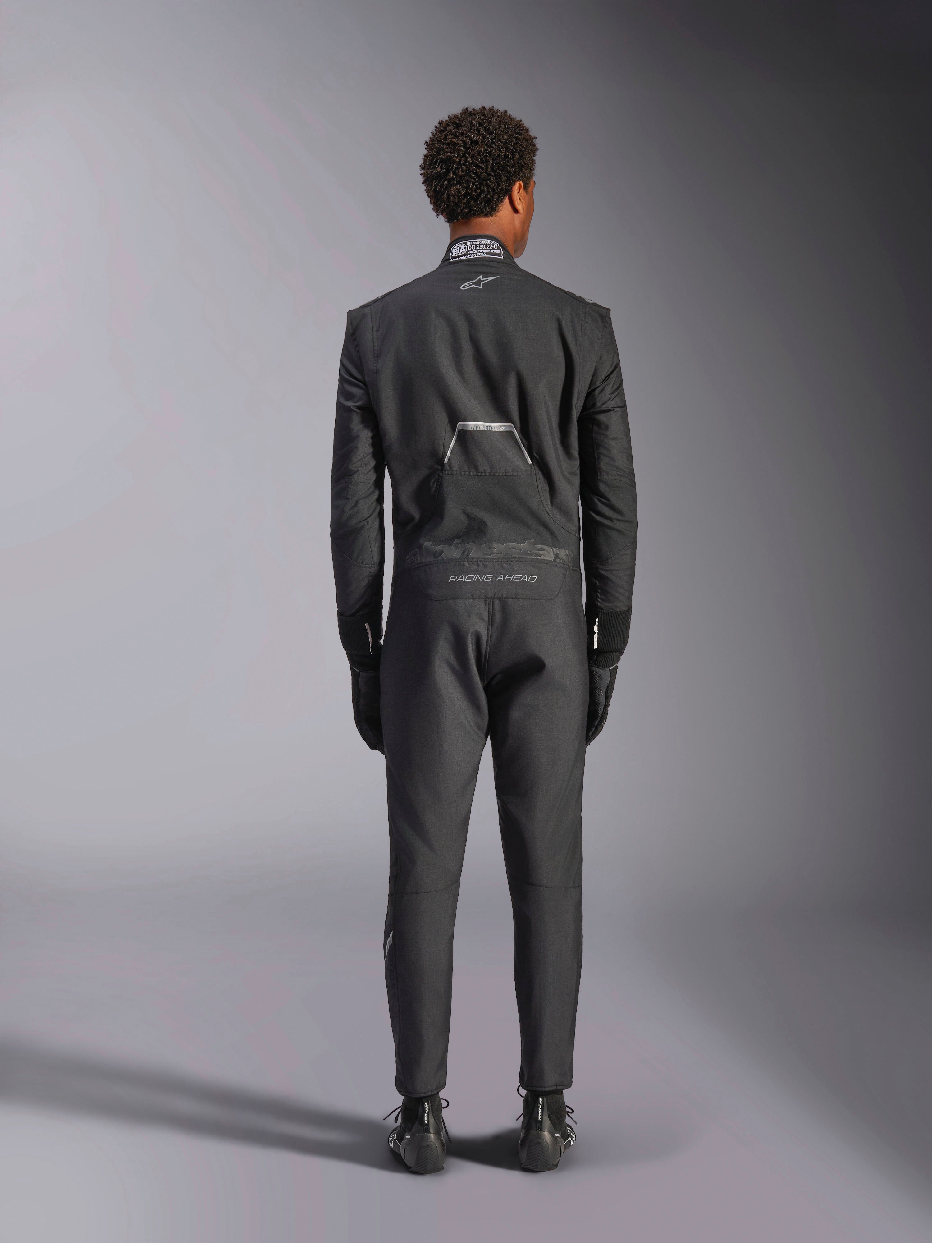 Alpinestars Hypertech V3 Anzug, Schwarz Dark Shadow, Rückansicht eines professionellen einteiligen Auto-Rennanzugs, mit FIA-Zertifizierungsetikett am Kragen und „Alpinestars“- sowie „RACING AHEAD“-Branding am unteren Rücken, getragen mit passenden schwarzen Rennhandschuhen und Stiefeln.