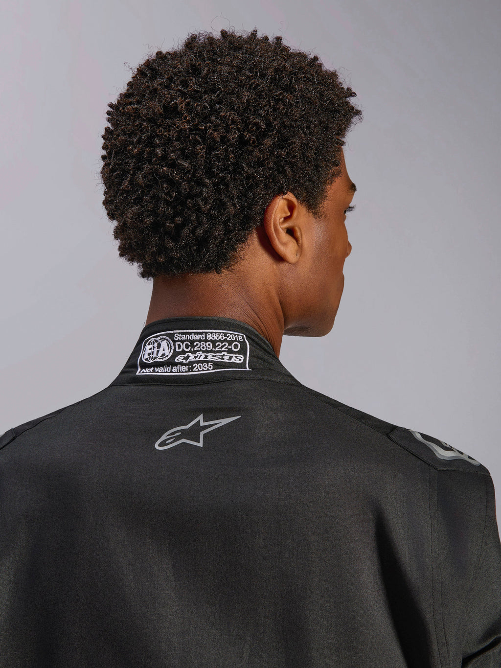 Alpinestars Hypertech V3 Anzug, Black Dark Shadow, Nahaufnahme der Rückansicht des Kragens mit FIA 8856-2018 Zertifizierungsetikett und Rücken-Logo, professioneller leichter Rennanzug mit athletischer Passform