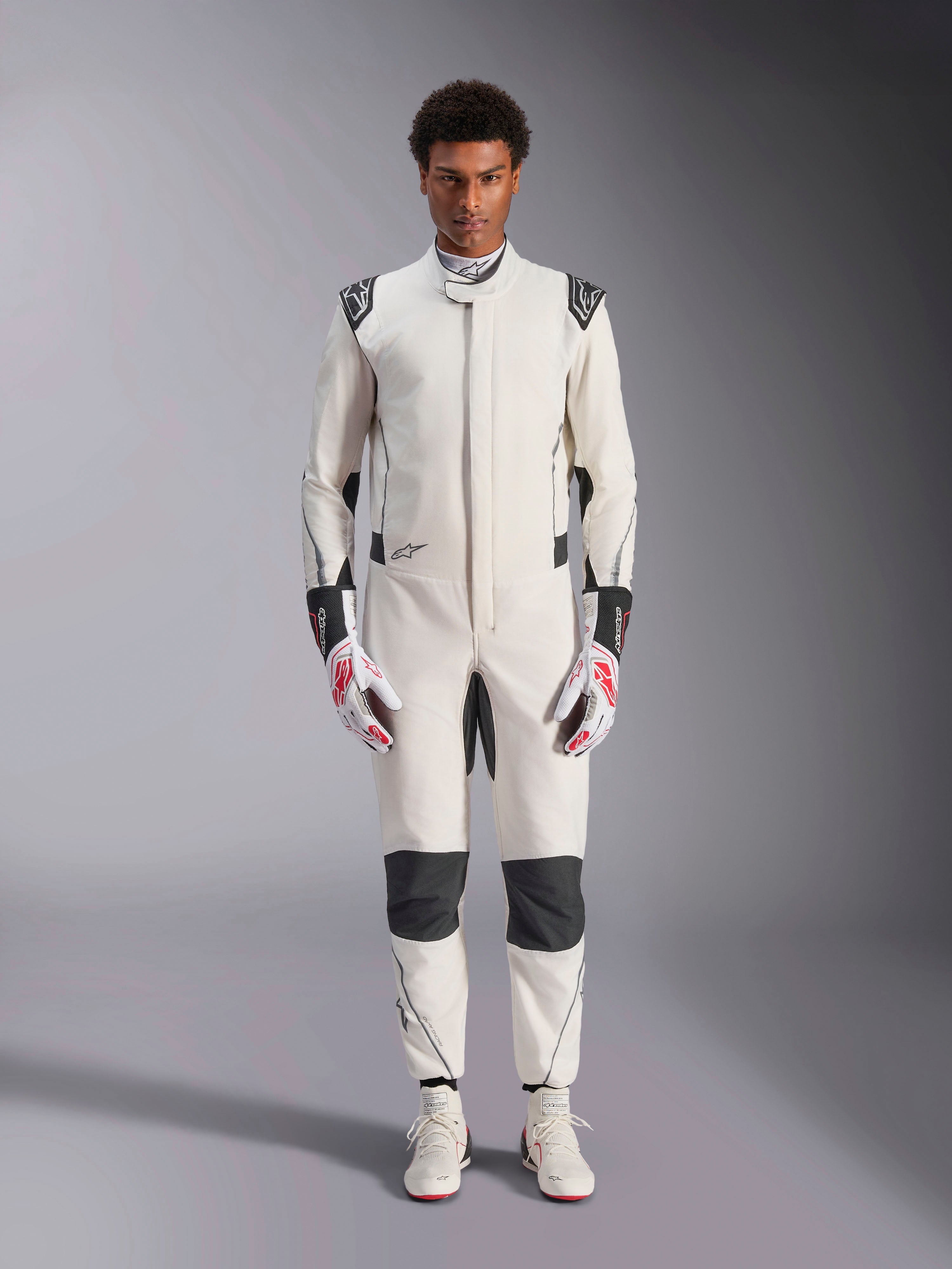 Alpinestars Hypertech V3 Suit, Professional Auto Racing Suit, White Black and Silver, worn by model with red and white gloves and matching white racing shoes, featuring black contrast panels and Alpinestars logos, athletic slim fit design