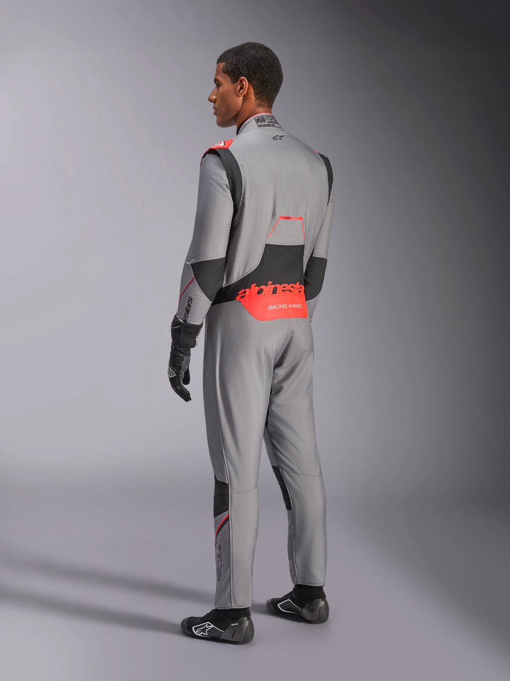 Alpinestars Hypertech V3 Suit in Mid Gray Black Red Fluo, rear three-quarter view, featuring bold red Alpinestars branding on the lower back, black stretch panels, and a sleek athletic fit for professional auto racing.
