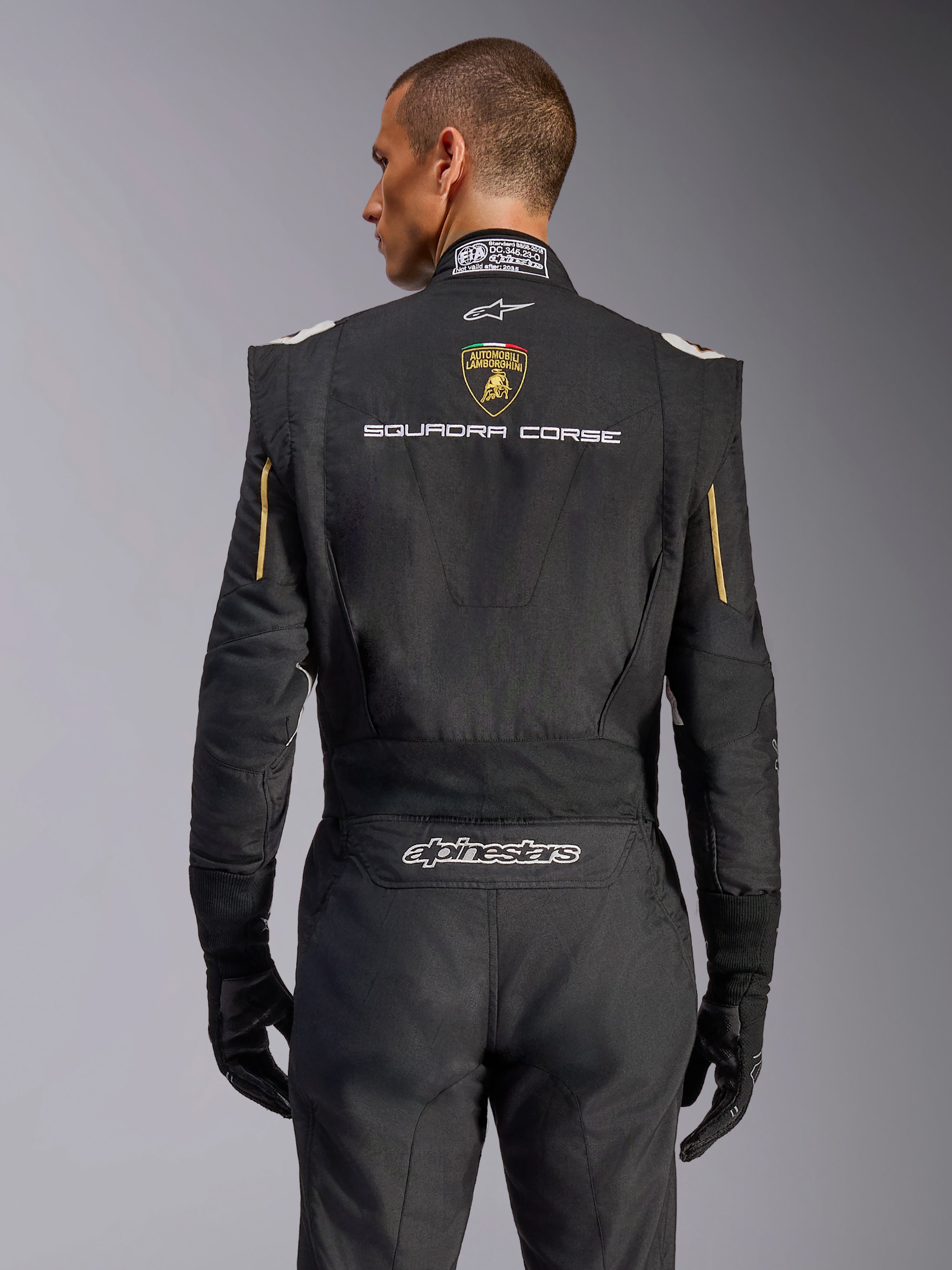 Rückansicht des Alpinestars Limited Edition Lamborghini GP Tech V4 Anzugs, Schwarz mit Gold-Akzenten, mit Automobili Lamborghini Wappen und „SQUADRA CORSE“-Schriftzug auf dem Rücken, professioneller FIA-zertifizierter Rennanzug für den Automobilsport