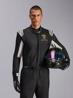 Alpinestars Limited Edition Lamborghini GP Tech V4 Anzug, Autorennanzug, Schwarz, Silber und Gold, getragen von einem Modell, das einen Carbon-Helm mit irisierendem Visier hält, mit Lamborghini Squadra Corse Branding und weißen Schulterakzenten