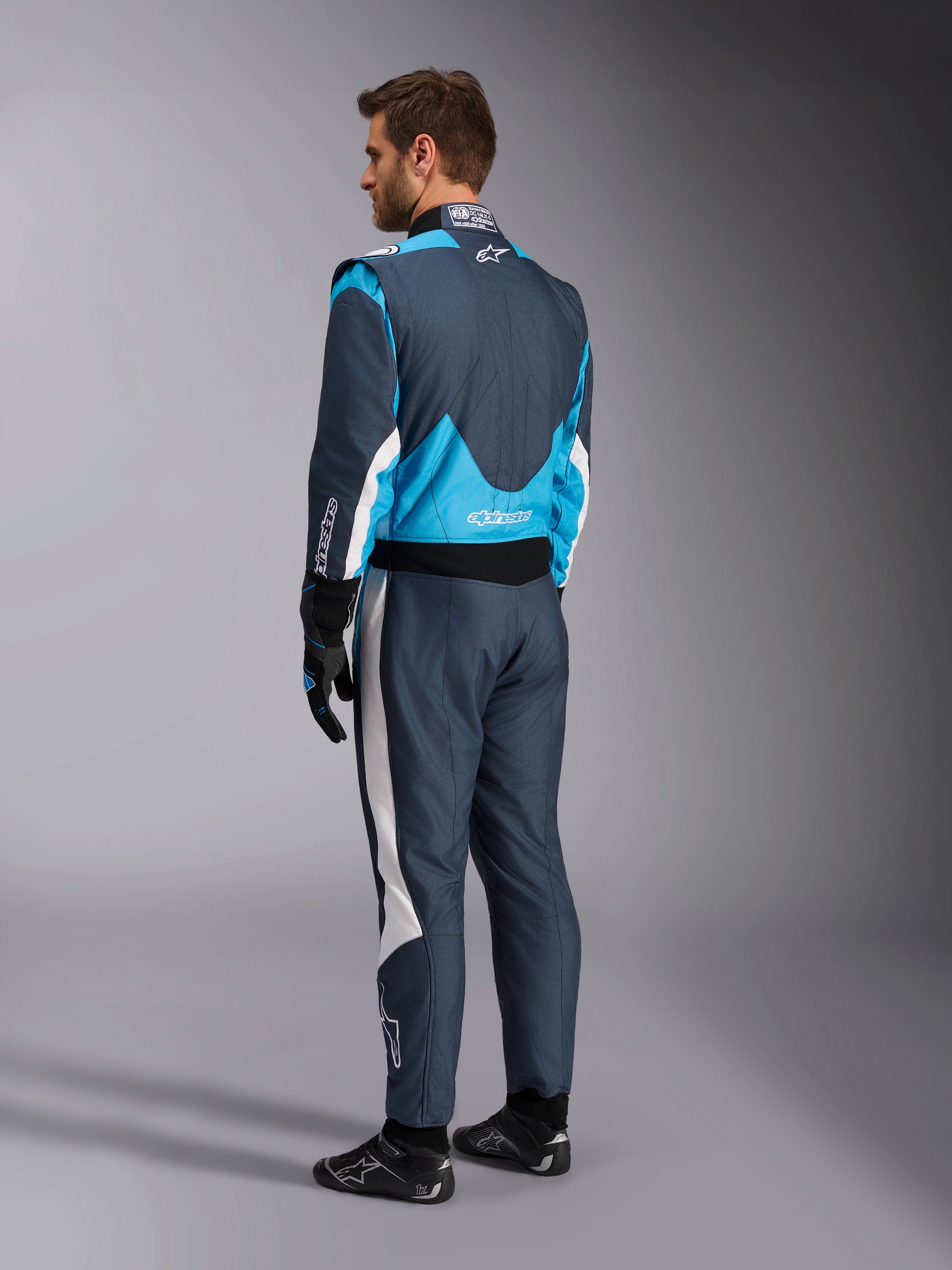 Alpinestars GP Pro Comp V2 FIA Auto Racing Suit in Asphalt and Cyan blue, rear view on a model with professional racing gear.