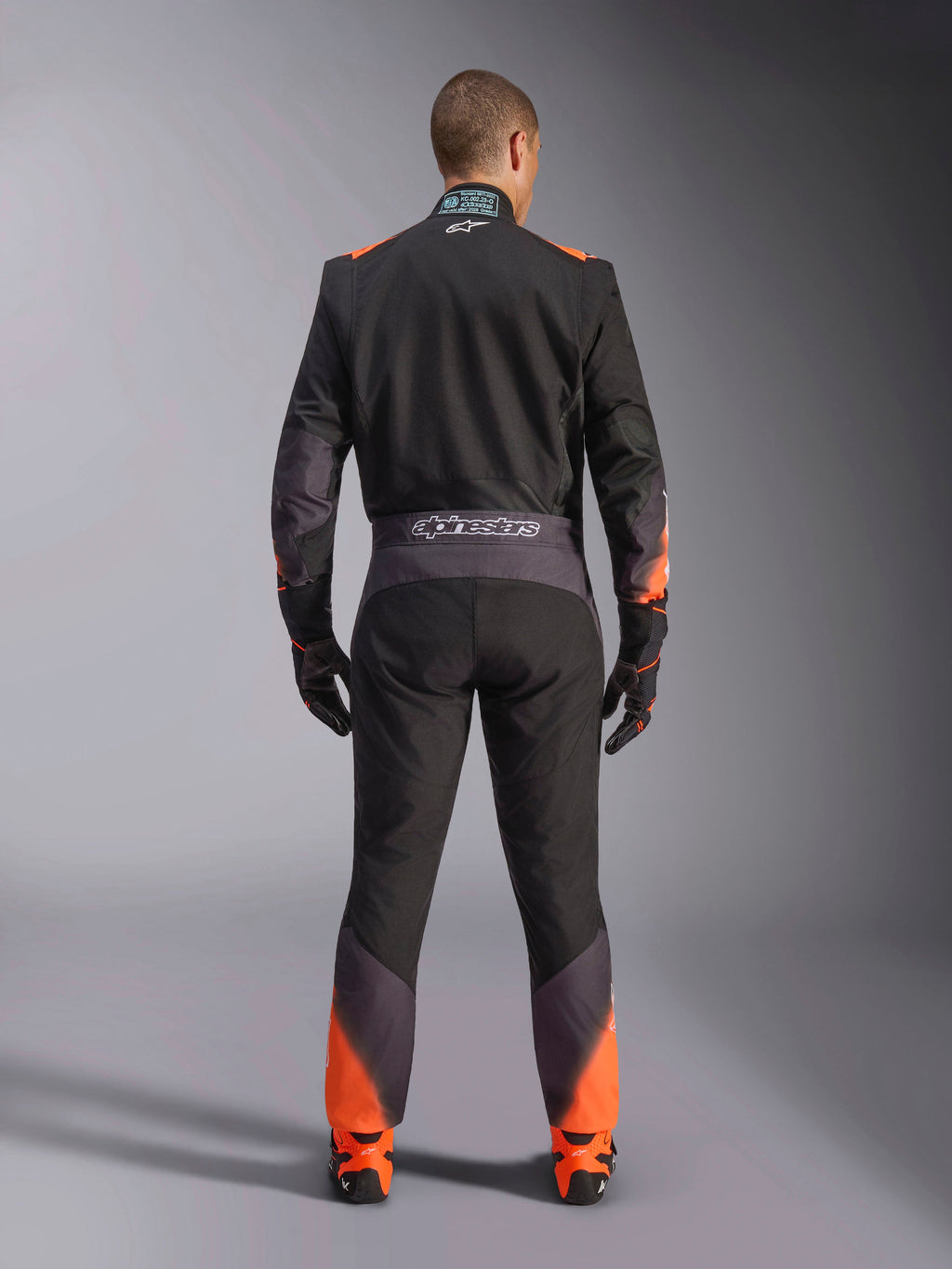 Alpinestars KMX-5 V3 Suit, men's black and orange fluo one-piece karting suit, FIA certified, rear view showing branding.