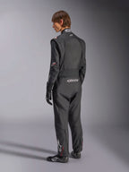 Alpinestars GP Tech V4 Anzug, Automobil-Rennanzug, Schwarz mit weißen Akzenten, Rückansicht eines Modells, das den Anzug mit Rennhandschuhen und Schuhen trägt, mit weißem Branding am unteren Rücken und am Bein, professionelle Motorsport-Schutzausrüstung
