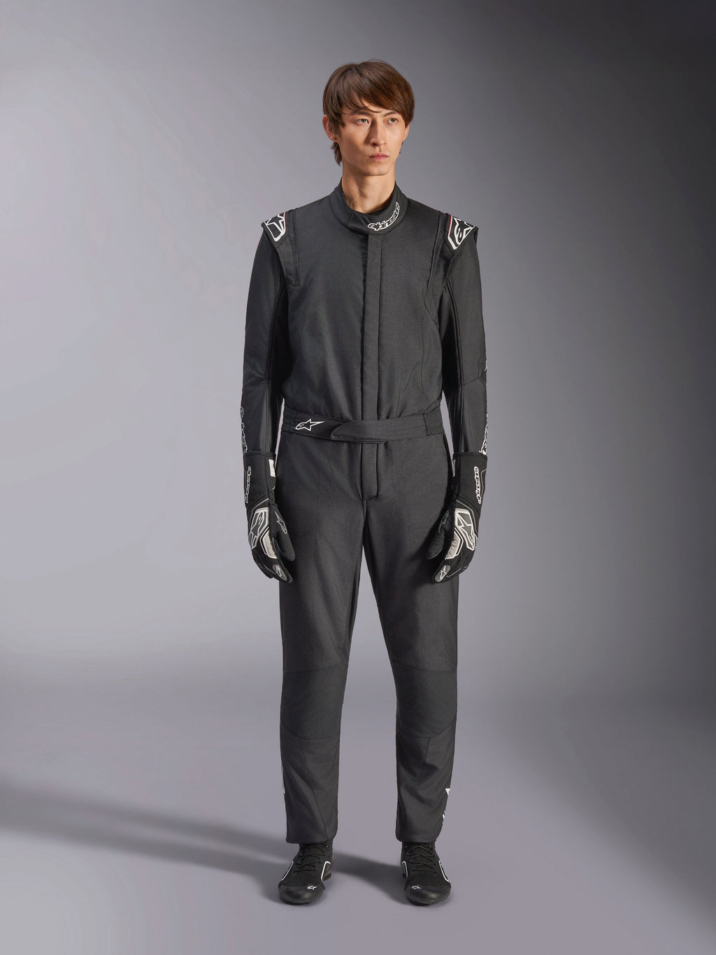 Alpinestars GP Tech V4 Anzug, Schwarz und Weiß, professioneller einteiliger Autorennanzug, getragen mit passenden schwarz-weißen Handschuhen und Rennschuhen, mit weißen Alpinestars-Logos an Schultern und Kragen, schlanke sportliche Passform für Motorsport-Wettbewerbe