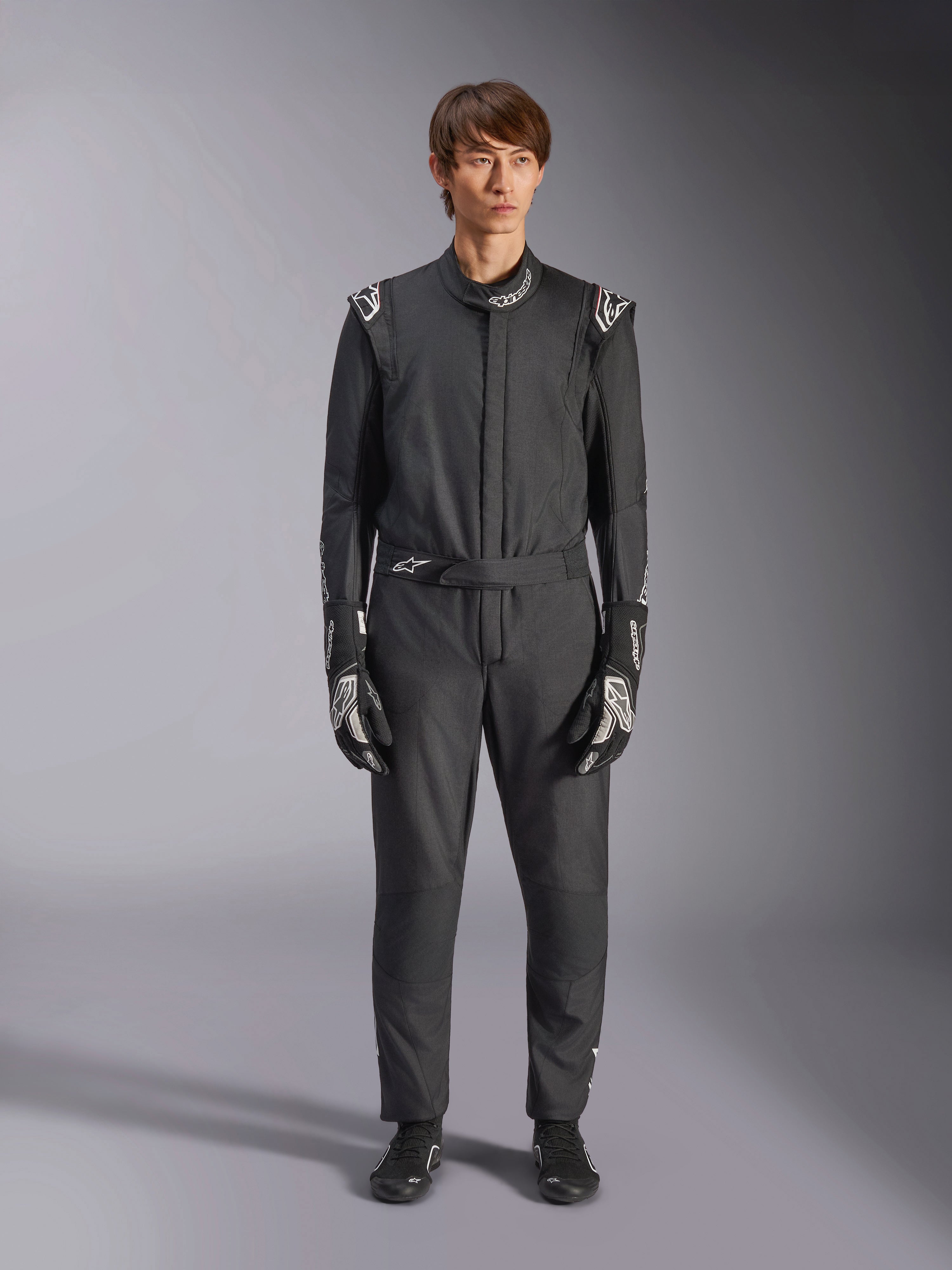 Alpinestars GP Tech V4 Anzug, Schwarz und Weiß, professioneller einteiliger Autorennanzug, getragen mit passenden schwarz-weißen Handschuhen und Rennschuhen, mit weißen Alpinestars-Logos an Schultern und Kragen, schlanke sportliche Passform für Motorsport-Wettbewerbe