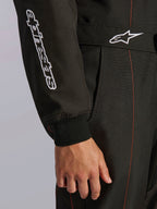 Nahaufnahme des Alpinestars KMX-9 V3 Anzugs in Schwarz und Rot Fluo, mit weiß besticktem Alpinestars-Branding am Ärmel, einem Strickbündchen am Handgelenk und einem Taillengürtel mit dem Astars-Logo und roten Kontrastnähten.