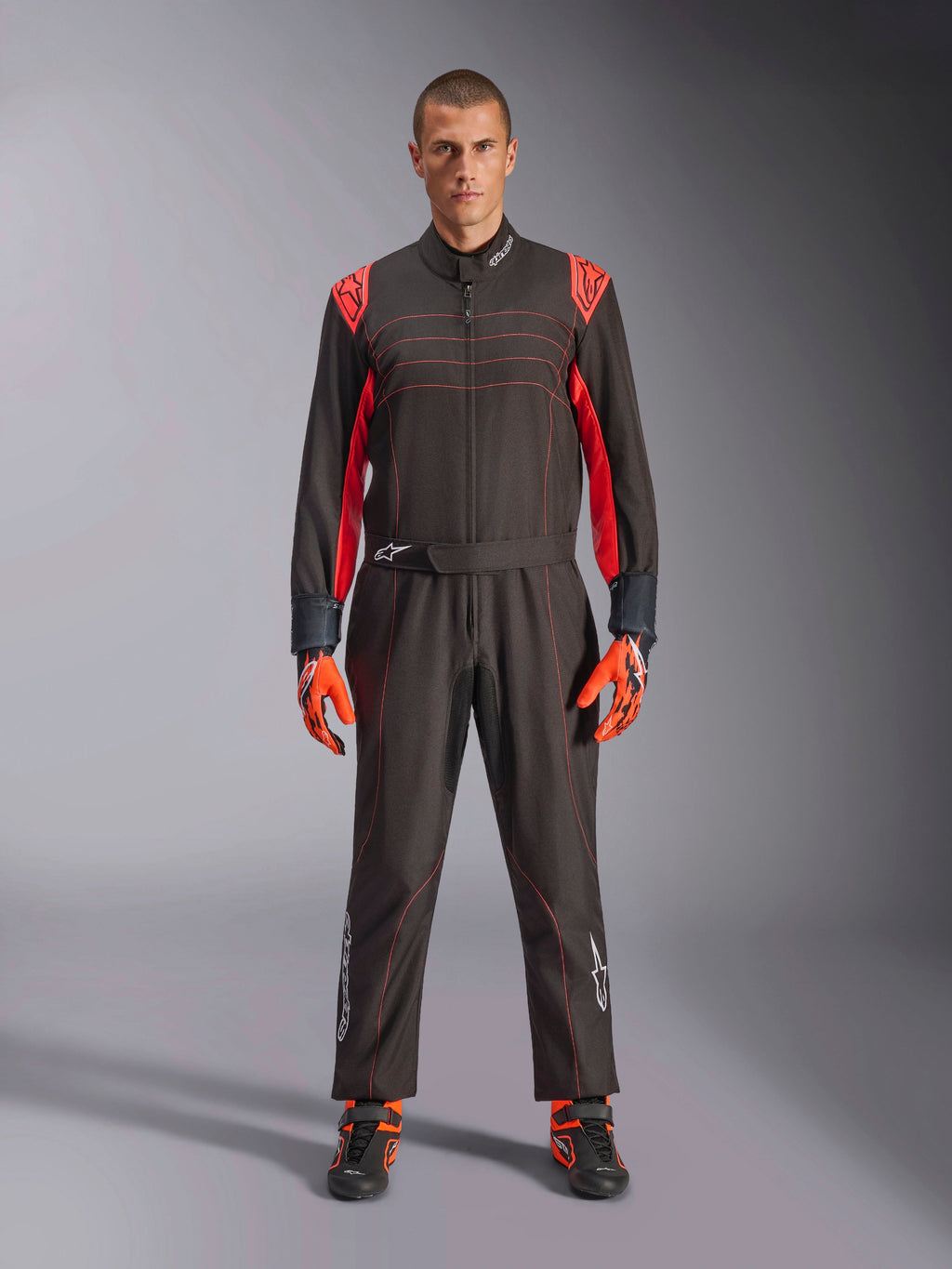 Alpinestars KMX-9 V3 Kart-Anzug, Schwarz und Fluo-Rot, einteiliger Rennanzug getragen mit farblich passenden Handschuhen und Stiefeln, mit leuchtend roten Schulterakzenten und Nähten, Alpinestars-Logo an den Unterschenkeln, schnittiges Motorsport-Design für den Rennsport