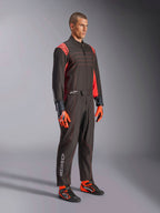 Alpinestars KMX-9 V3 Anzug, Karting-Anzug, Schwarz Rot Fluo, getragen von einem Modell mit orangefarbenen Handschuhen und schwarzen Rennschuhen, mit roten Nähten, Schulterakzenten und weißen Logos, athletisches Design für professionellen Rennsport
