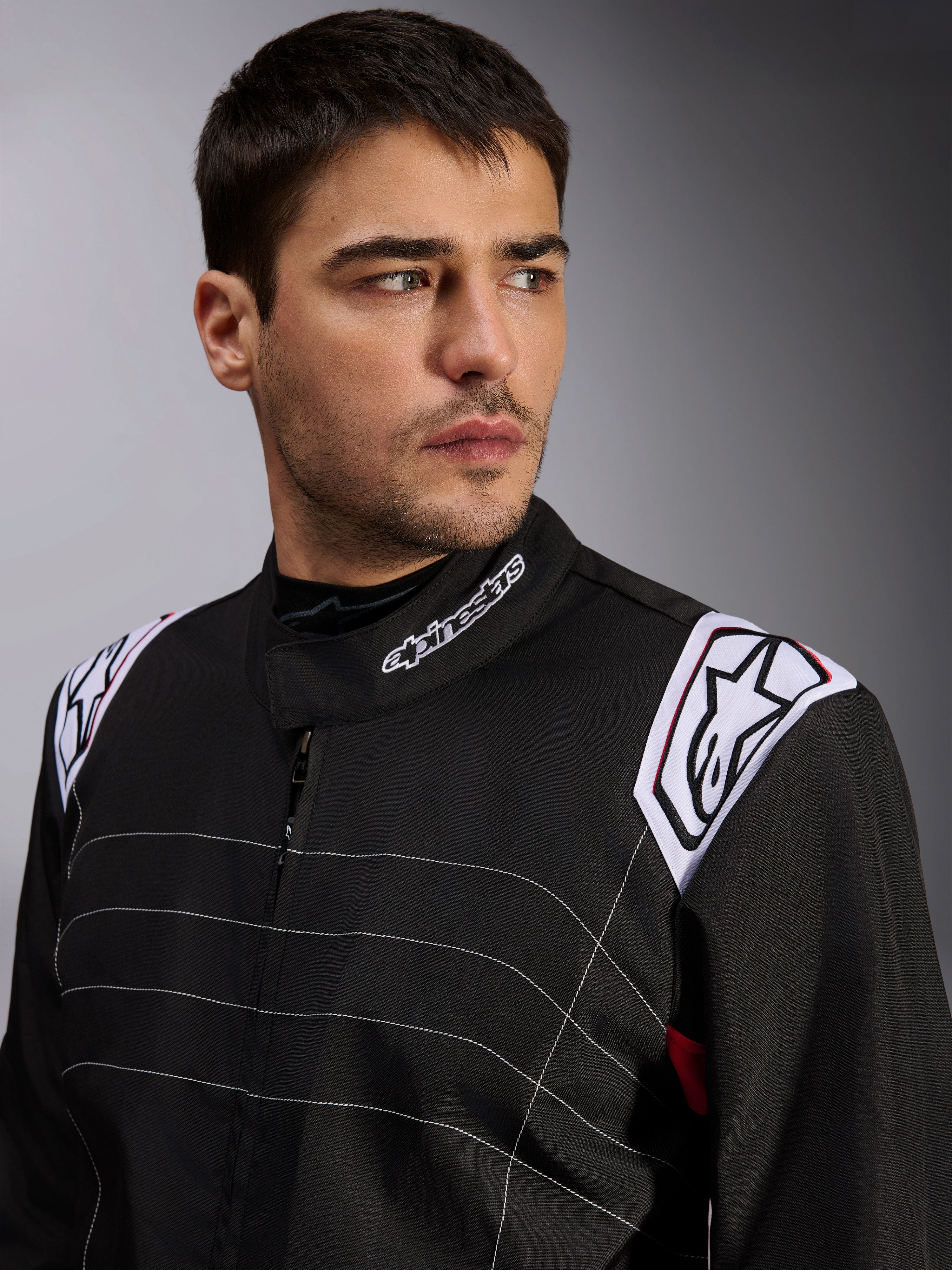 Alpinestars KMX-9 V3 Anzug, schwarzer Kart-Anzug, getragen von einem männlichen Model, Nahaufnahme von Brust und Schultern mit weißem Branding am Kragen und an den Epauletten, mit weißen Ziernähten und einem professionellen Motorsport-Design
