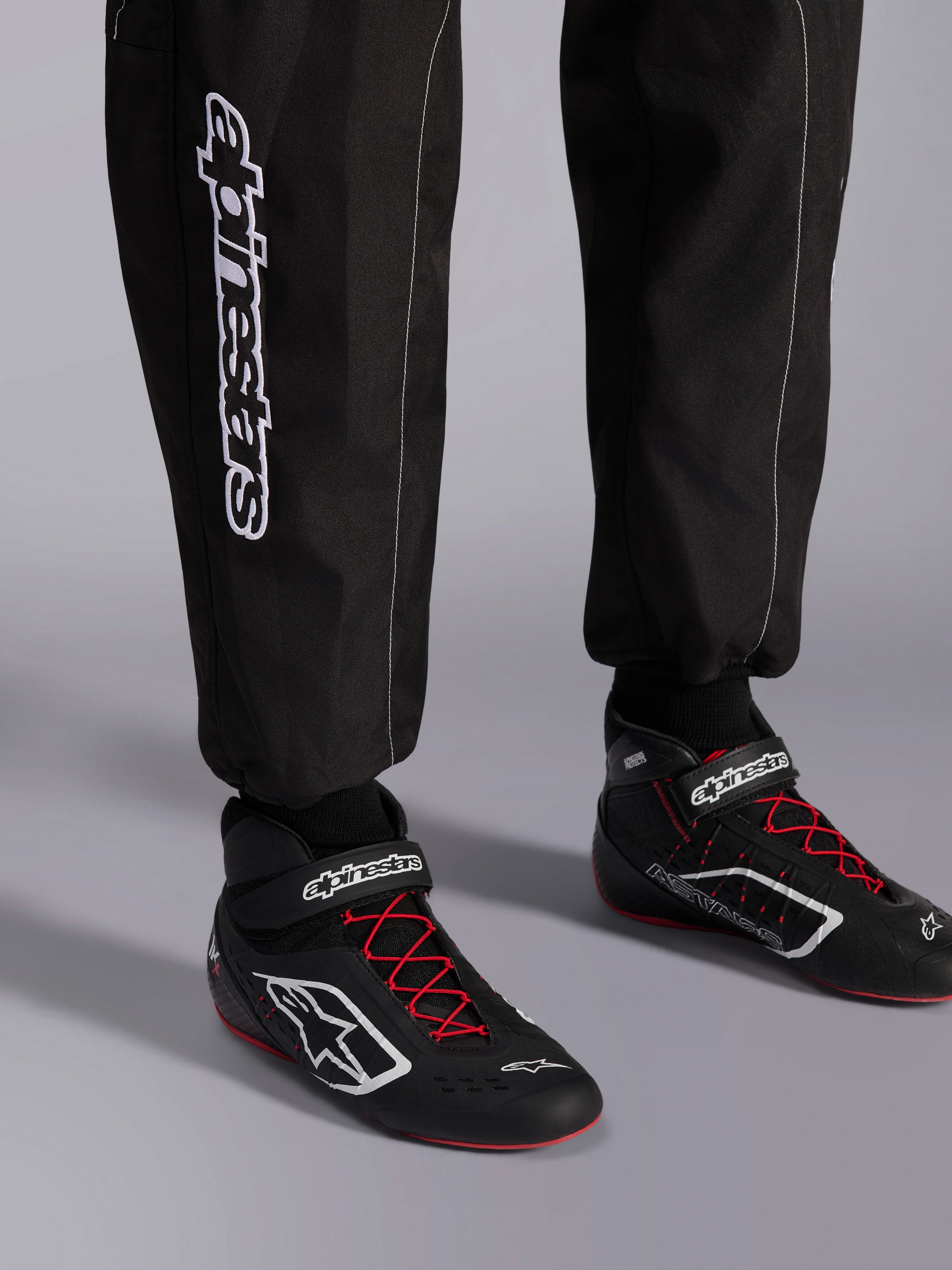 Alpinestars KMX-9 V3 Anzug, Kart-Anzug, Schwarz, Rot und Weiß, Detailansicht der Unterschenkel und Karting-Stiefel, weißes Alpinestars-Branding an der Seite, schwarze Schuhe mit roten Schnürsenkeln und weißen Akzenten, professionelle Motorsport-Rennausrüstung.