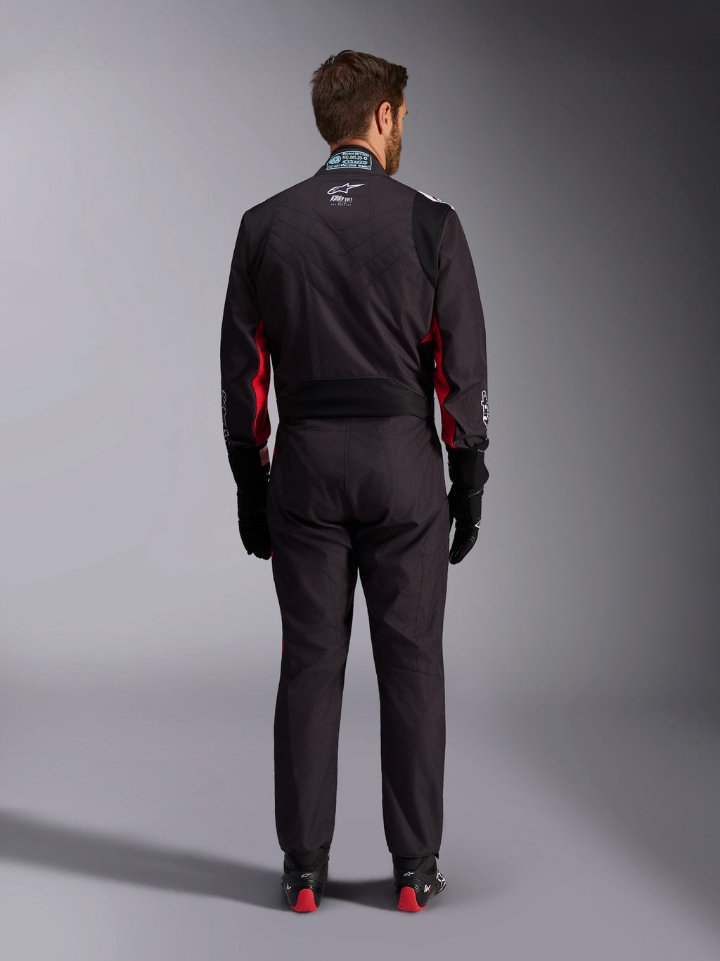 Alpinestars KMX-9 V3 Graphic 3 Anzug, Kart-Anzug, Schwarz und Rot, Rückansicht mit Lenden-Stretcheinsatz und FIA-Zertifizierungsetikett am Kragen, kombiniert mit schwarzen Rennhandschuhen und rot akzentuierten Stiefeln