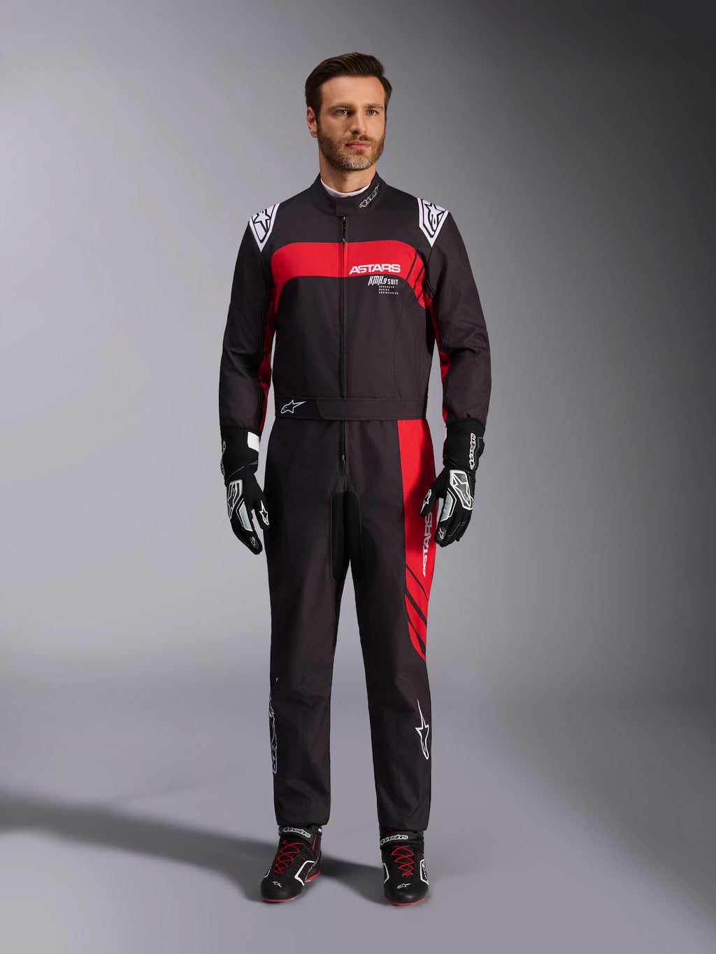 Alpinestars KMX-9 V3 Graphic 3 Anzug, Karting-Anzug, Schwarz und Rot, Ganzkörper-Frontansicht an einem Modell, mit markanten roten Grafik-Einsätzen und weißem Branding, kombiniert mit schwarzen Rennhandschuhen und Schuhen, professionelle Motorsport-Bekleidung.