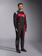 Männliches Modell im Alpinestars KMX-9 V3 Graphic 3 Anzug, Karting-Anzug, Schwarz und Rot, mit weißen Schulter-Epauletten und rotem Brust-Logo, kombiniert mit schwarzen Rennhandschuhen und Schuhen mit roten Schnürsenkeln, professionelle Motorsportbekleidung