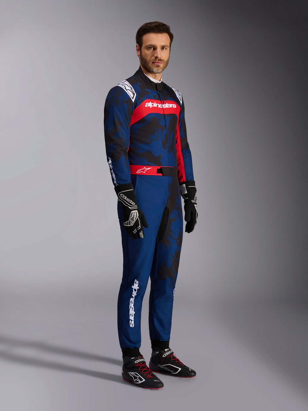 Model wearing the Alpinestars KMX-9 V3 Graphic 5 Suit in Navy Red, full-body shot including black karting gloves and black racing shoes, navy blue suit with dark camo-style graphics and a prominent red chest panel with white branding, professional karting protective gear