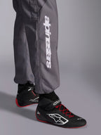 Alpinestars KMX-9 V3 Graphic 5 Anzug, Kart-Anzug, Dunkelgrau, Nahaufnahme des Unterschenkels mit weißem vertikalem Alpinestars-Logo, getragen mit schwarz-roten Rennschuhen, strapazierfähiges Material für den Kart-Wettbewerb