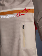 Alpinestars Maxdura Dual Jersey, Aluminum Walnut, Detailansicht des Mesh-Torsos, horizontaler orange-weißer Streifen mit rotem Logo, vertikale Brusttasche mit Reißverschluss, Adventure-Motorradbekleidung