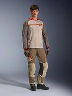 Model trägt das Alpinestars Maxdura Dual Jersey in Aluminum Walnut, mit einem grauen Mesh-Torso, braunen Ärmeln mit roten Bündchen und Brusttaschen mit Reißverschluss, kombiniert mit passender Offroad-Ausrüstung für Adventure-Fahrten.