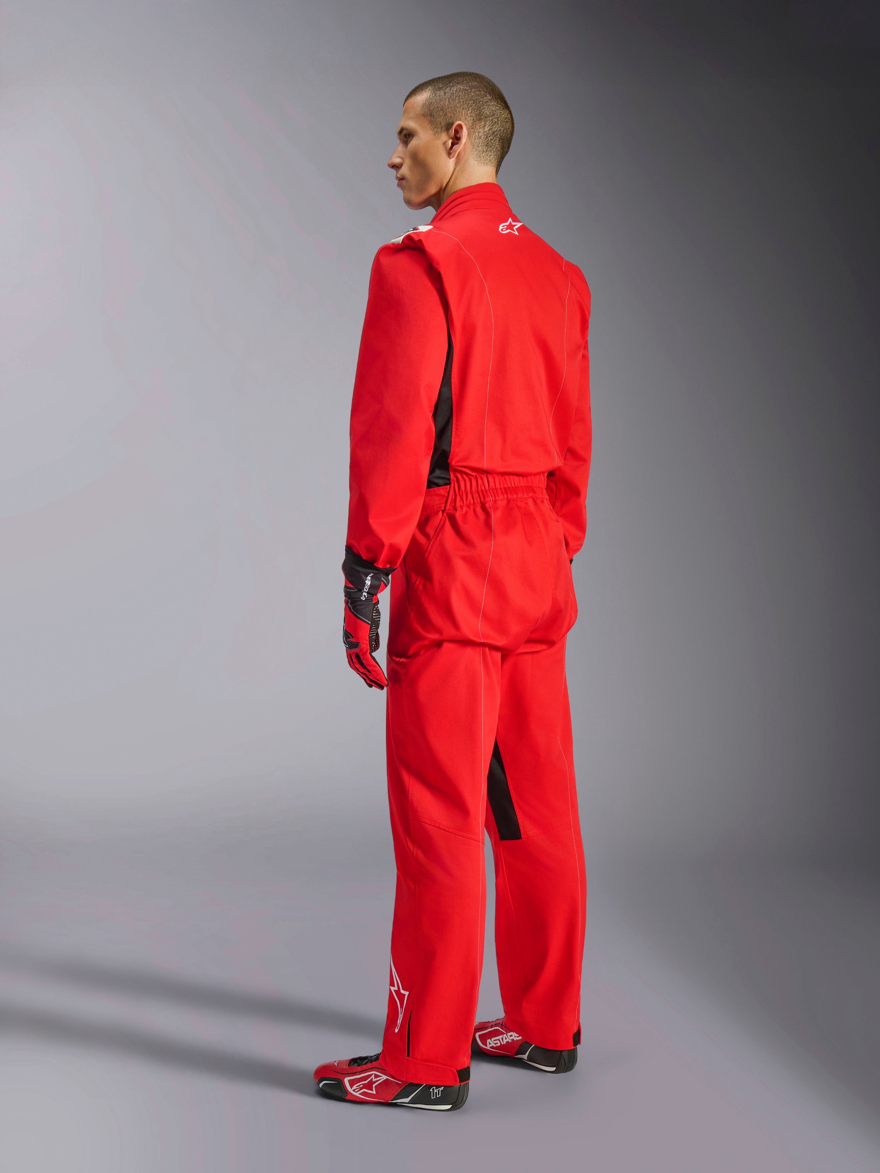 Alpinestars Kart Indoor V2 Anzug, roter Kart-Anzug, Dreiviertel-Rückansicht an einem Modell, getragen mit passenden roten Handschuhen und Rennschuhen, einlagige Poly-Baumwoll-Twill-Konstruktion, professionelle Motorsportausrüstung für Indoor-Kartfahren.